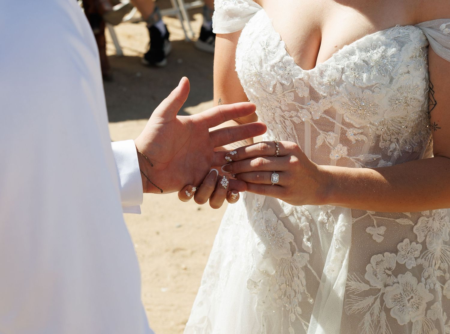 Bride and groom exchanging rings during outdoor beach wedding ceremony, close-up of hands in white lace dress.