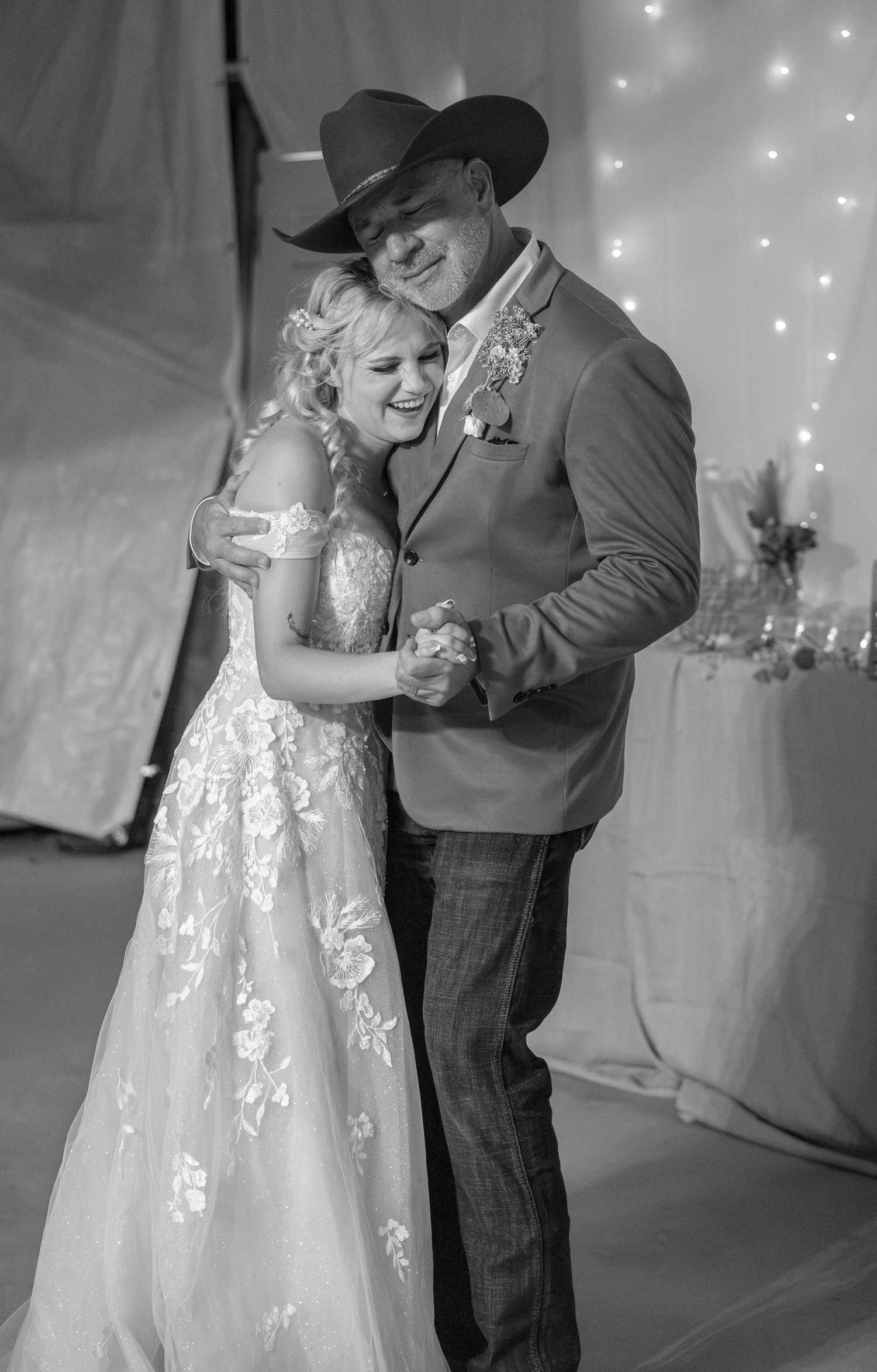 Bride and groom share a tender first dance in black and white, both wearing cowboy hats at their country wedding.