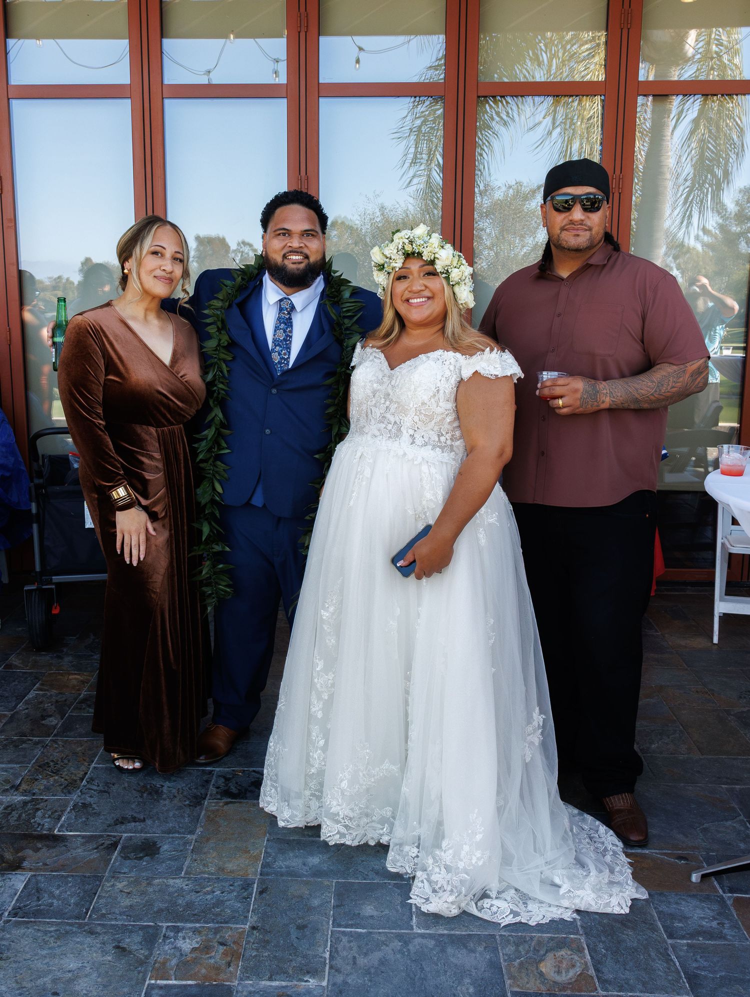 Bride in floral crown and lace gown poses with three guests outdoors at wedding celebration.