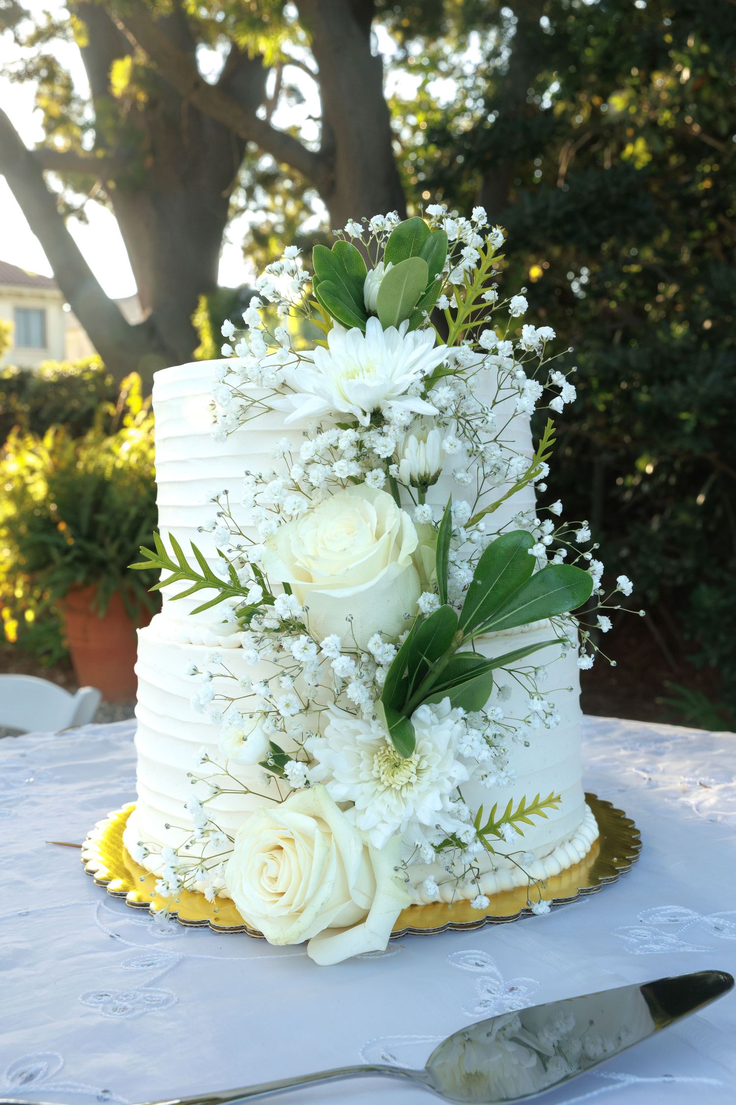 Elegant two-tier white wedding cake adorned with fresh white roses and greenery.