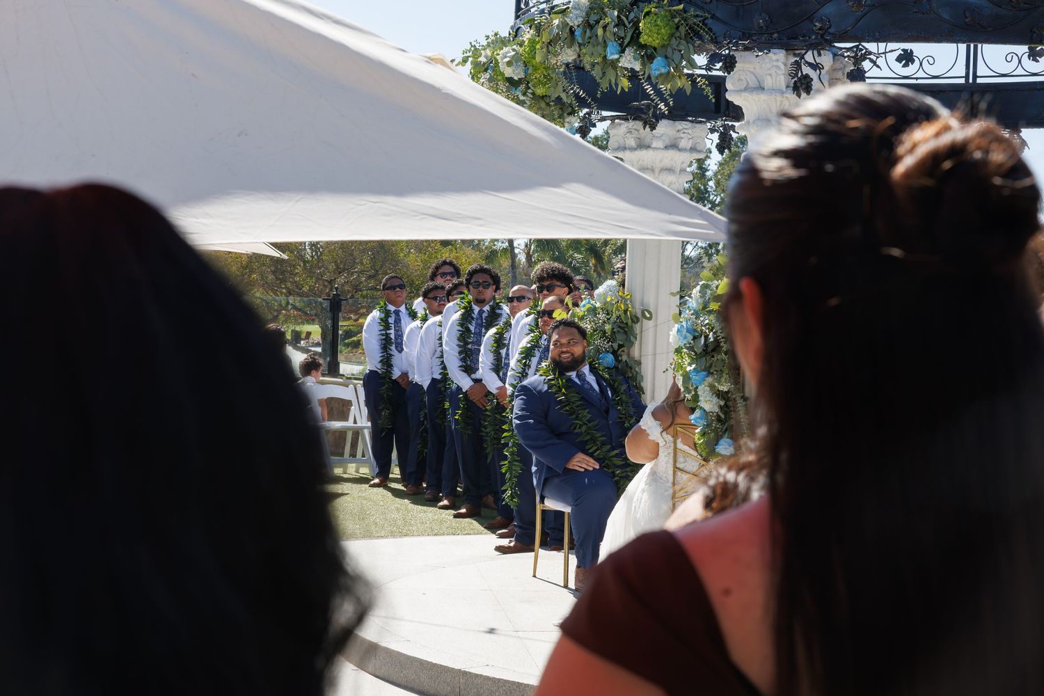 Military personnel in uniform stand at attention under a white tent canopy during an outdoor ceremony.