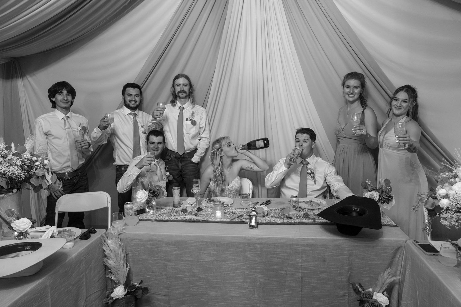 Wedding party poses at head table during reception in black and white photo.