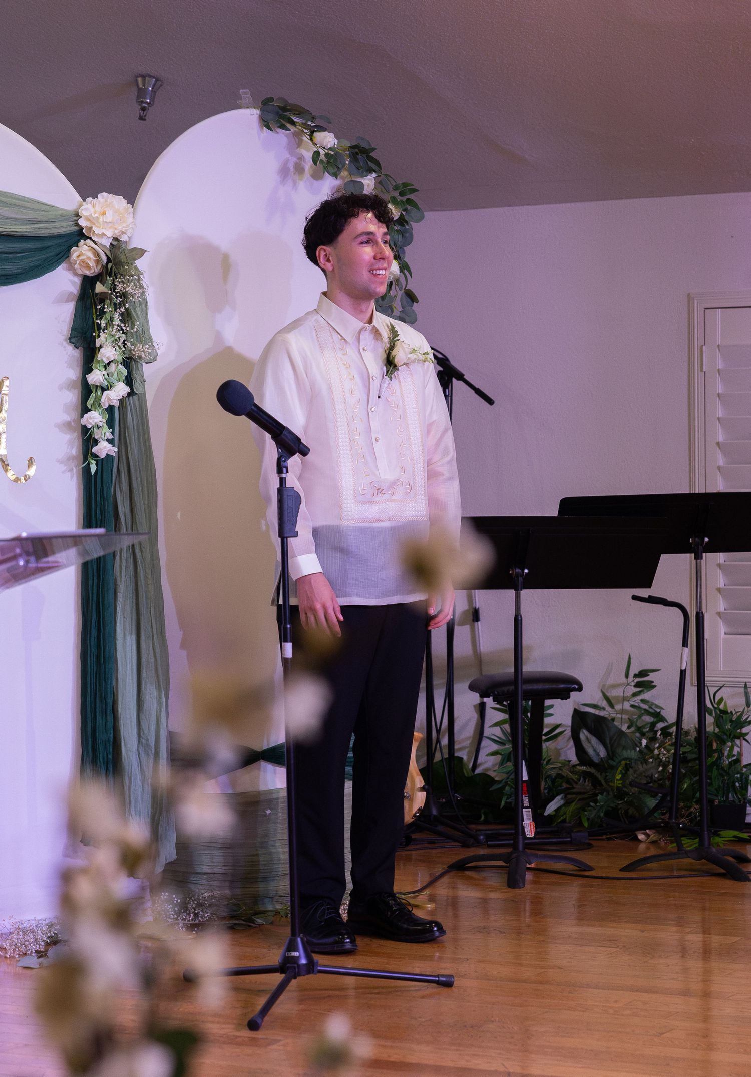 Young man in traditional barong tagalog stands at altar microphone during wedding ceremony decoration.