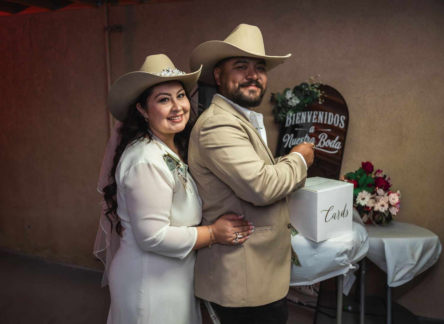 Couple in western cowboy hats poses at wedding reception near a Bienvenidos sign and card box.