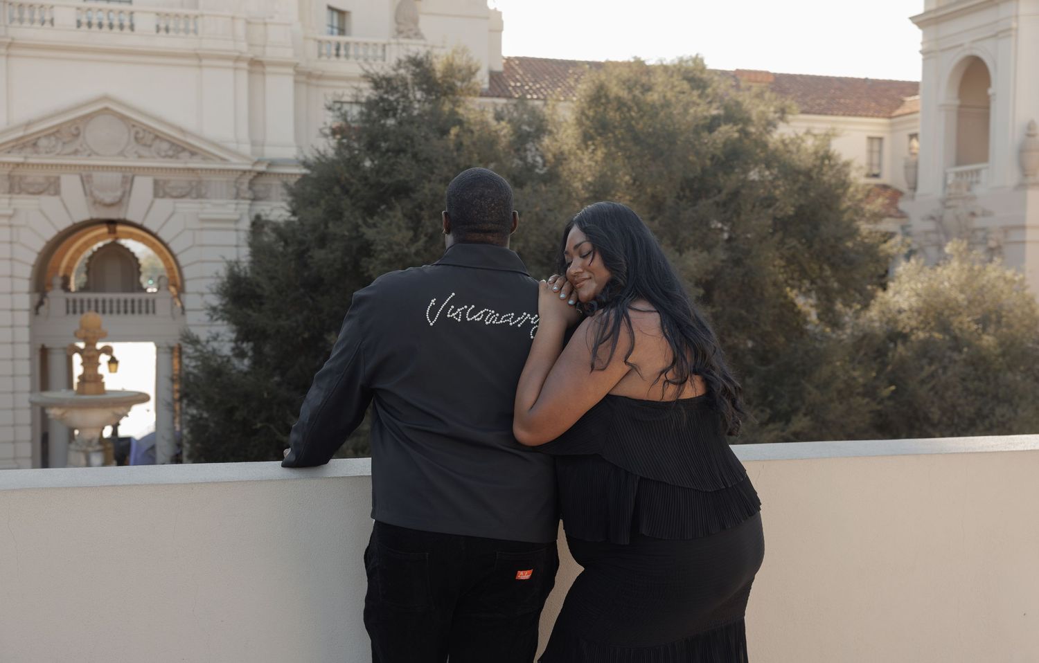 Couple in black outfits sharing a romantic moment on a rooftop overlooking an elegant building.