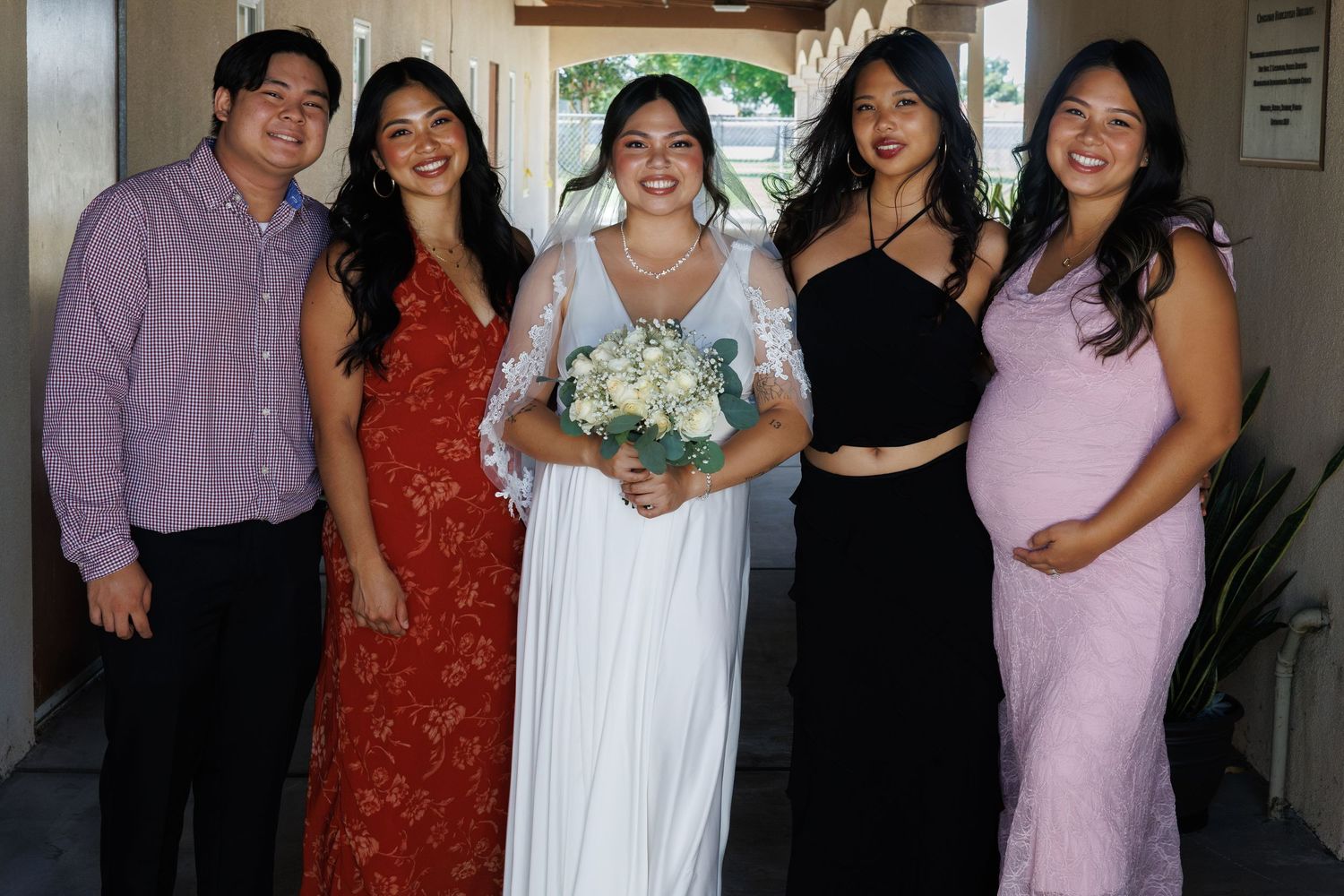 Bride in white gown poses with four wedding guests in colorful formal attire, holding a white bouquet.