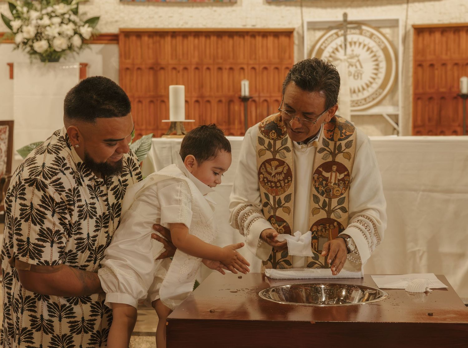 Priest performing a baptism ceremony with father and baby at the baptismal font.