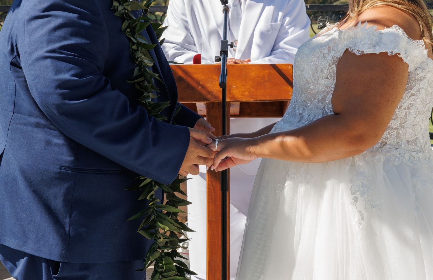 Bride and groom exchanging vows at outdoor wedding ceremony with officiant and wooden podium.