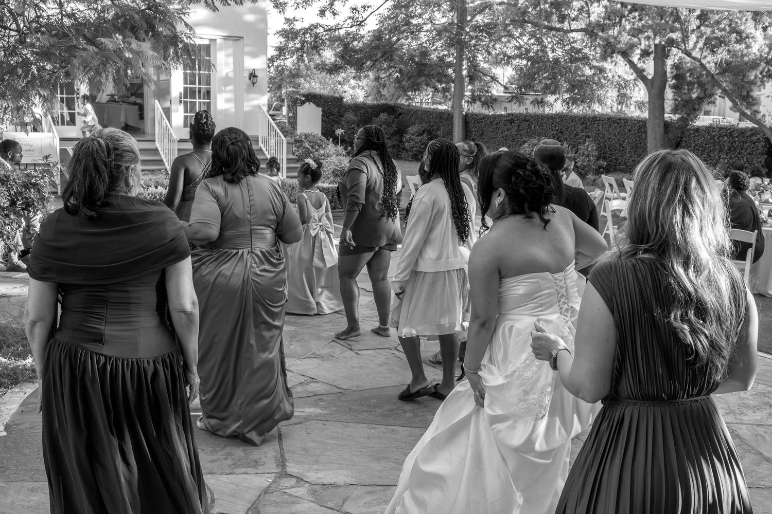 Wedding party walking outdoors in black and white photo, bridesmaids in long gowns following bride.