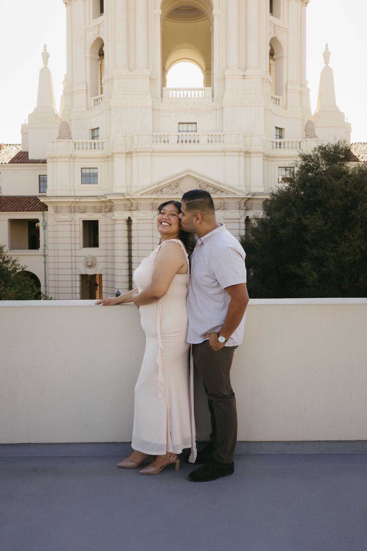 Couple sharing a romantic moment on a rooftop terrace with Pasadena City Hall architecture in the background.