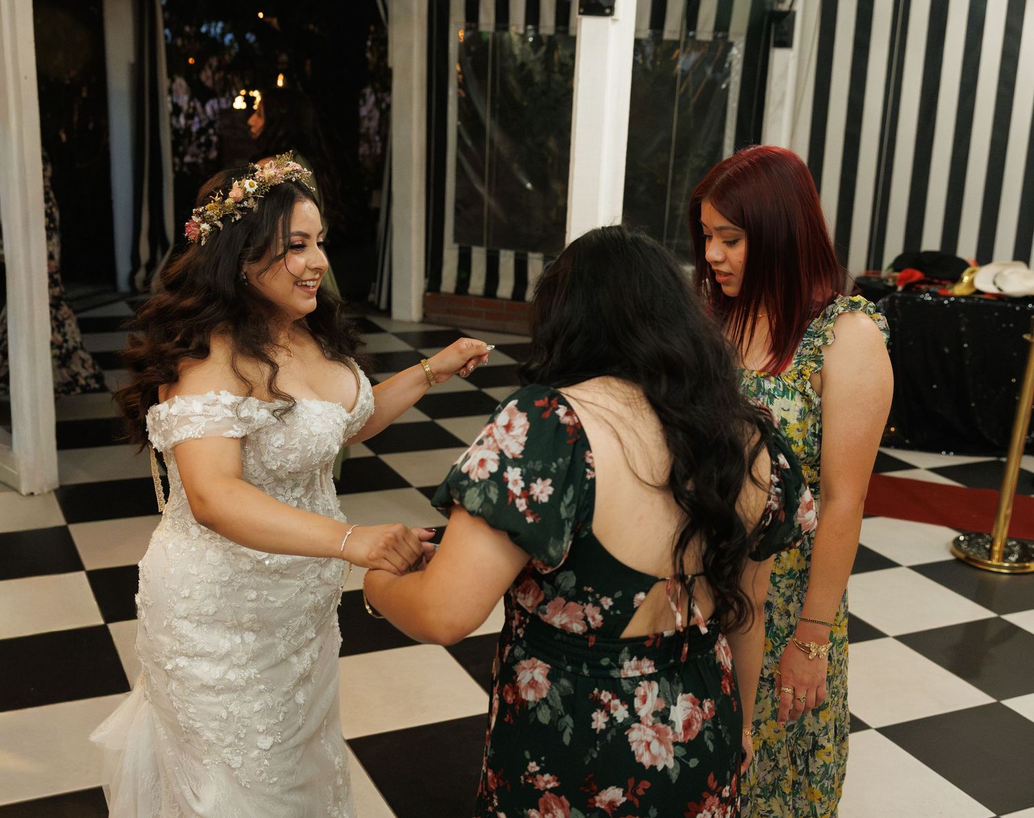 Bride in white gown with guests on black and white checkered dance floor at wedding reception.