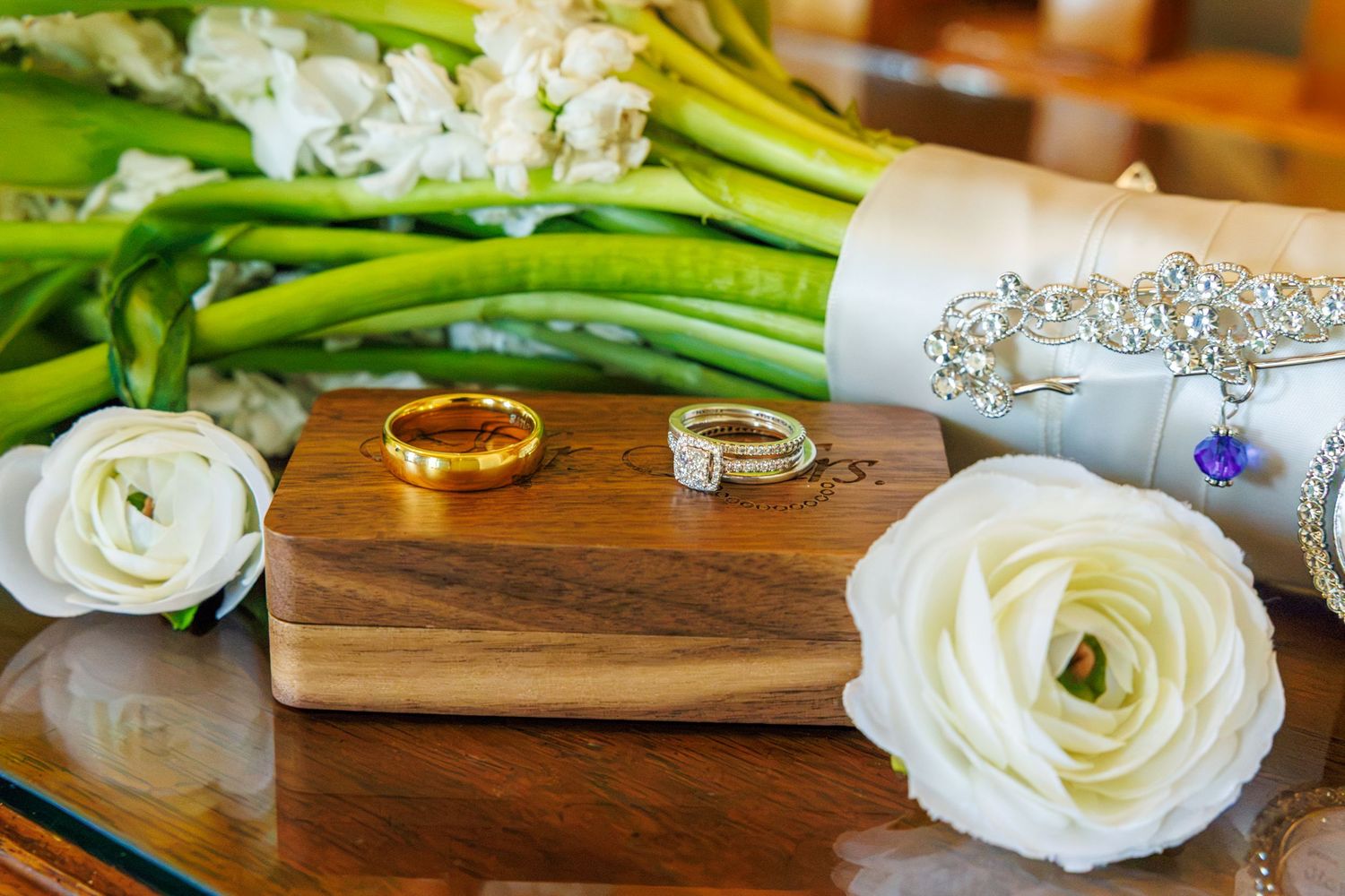 Wedding rings on wooden box with white roses and bridal bouquet arrangement.