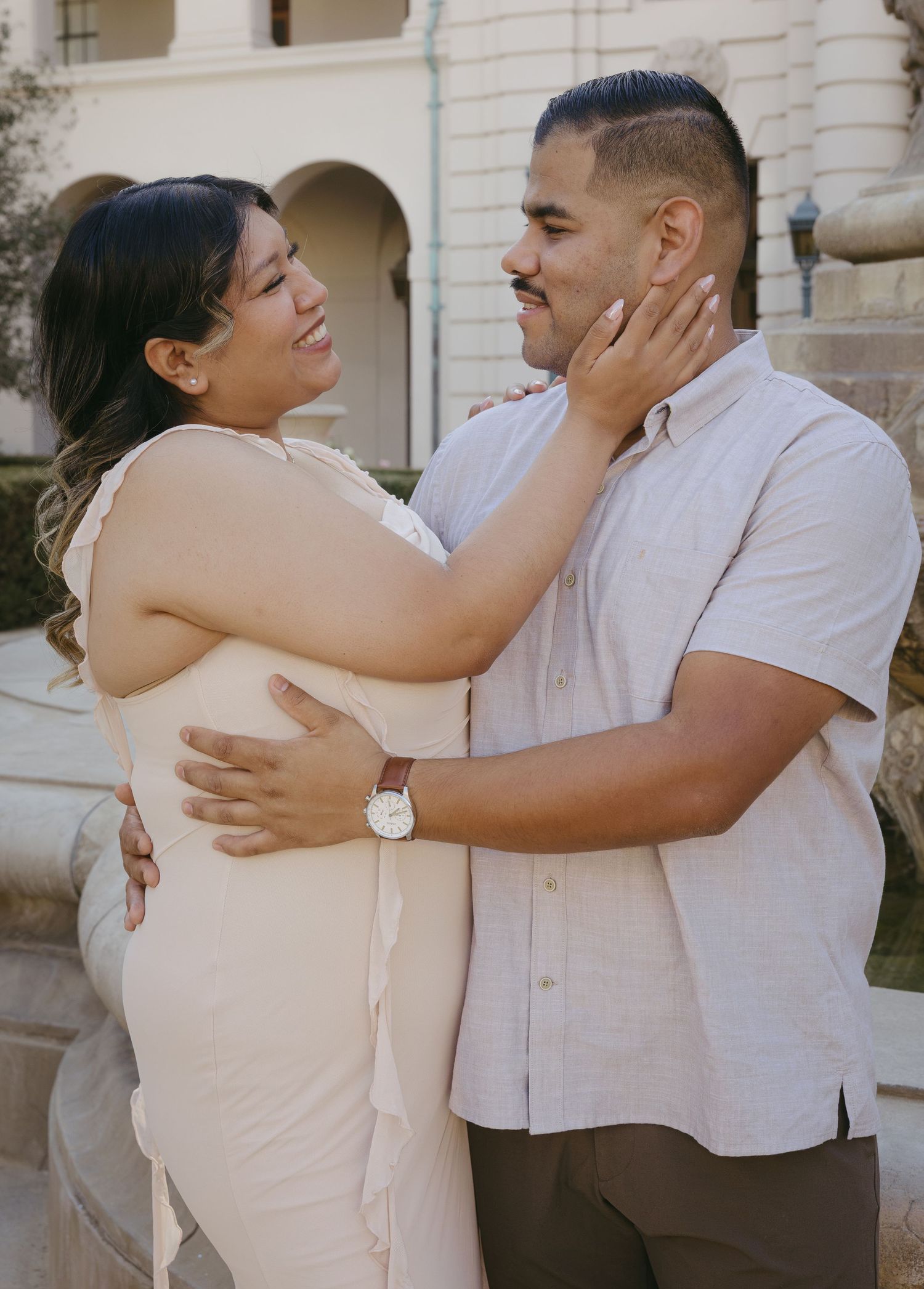 A couple embraces and smiles at each other outdoors, the woman touching the man's face tenderly.