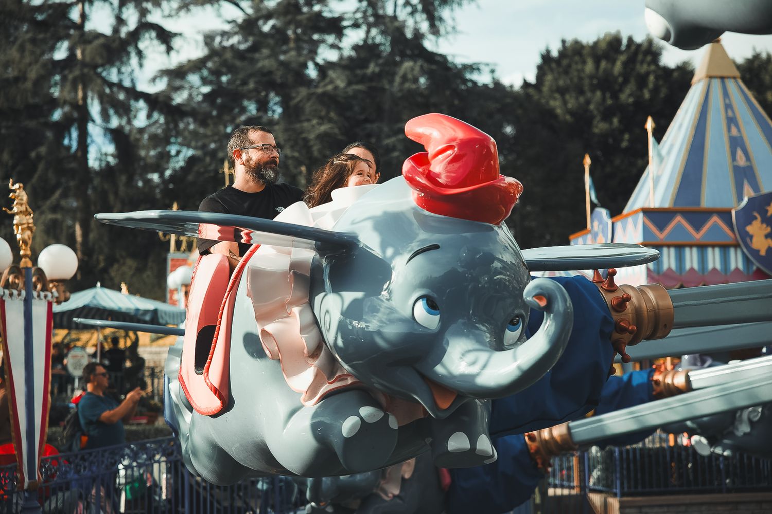 Family riding the Dumbo the Flying Elephant attraction at Disneyland on a sunny day.