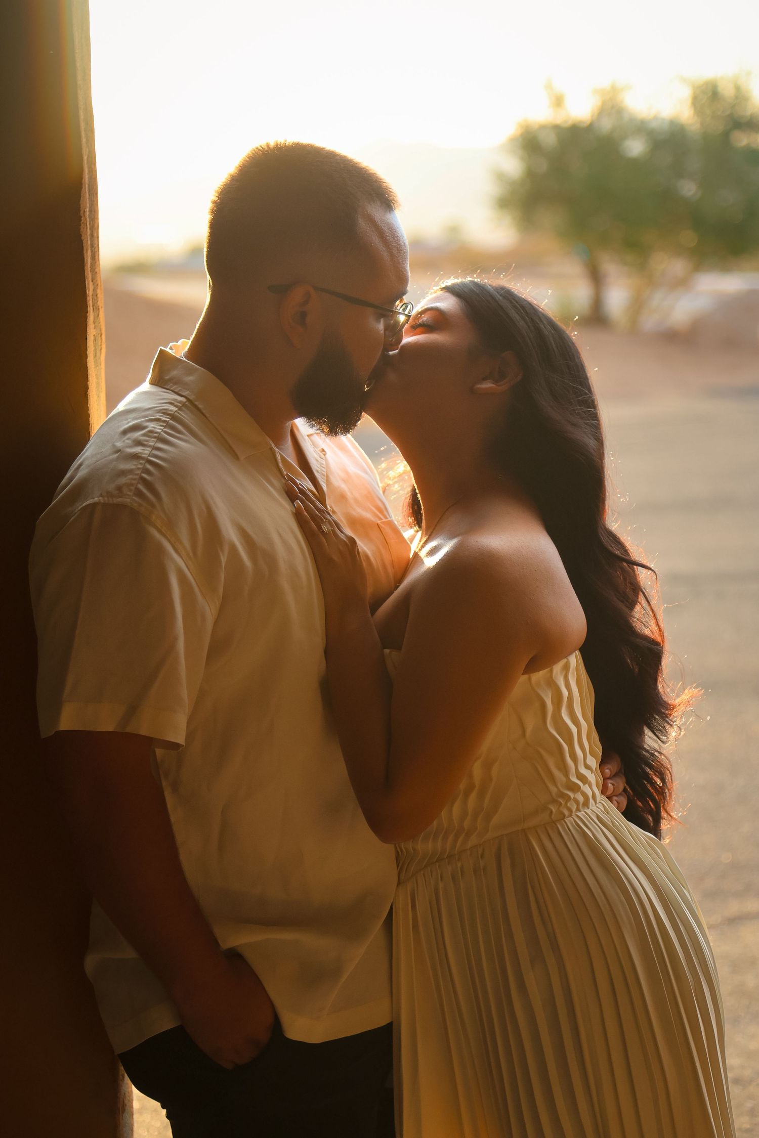 Couple sharing a romantic moment at golden hour, woman in yellow dress leaning toward bearded man in white shirt.