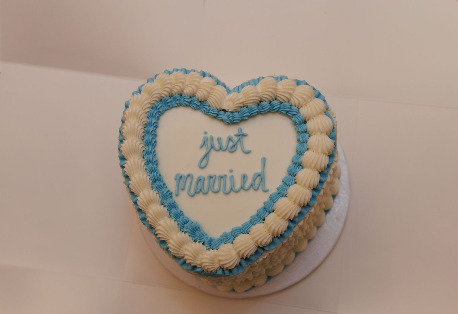 Heart-shaped wedding cake decorated with white rosettes and blue frosting reading just married.