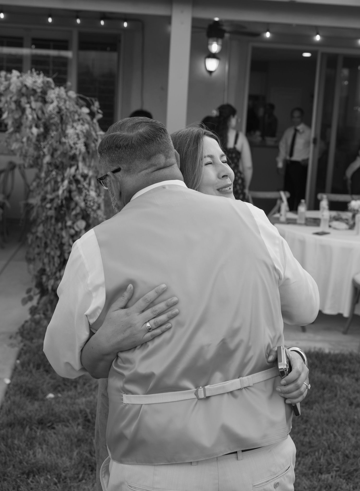Black and white photo of a couple sharing an emotional dance embrace at an outdoor wedding reception.