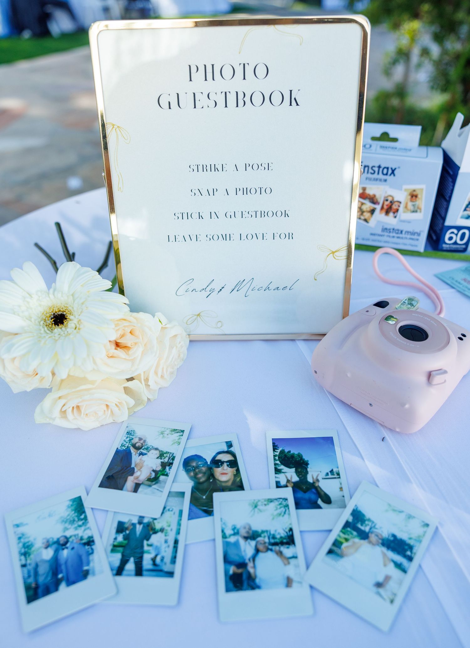 Wedding photo guestbook station with Instax camera, polaroid photos, and floral arrangement for Cody and Michael.