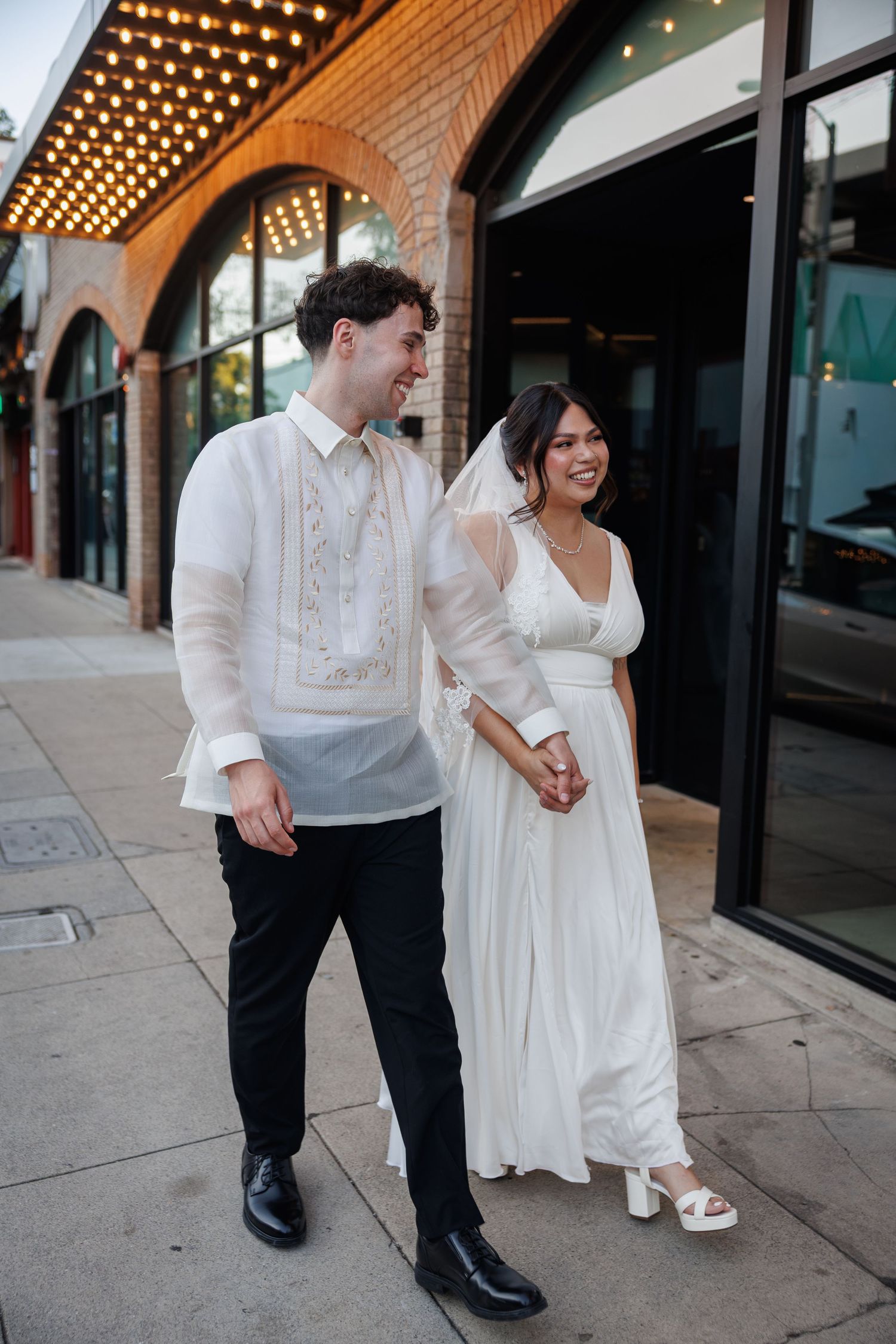 Newlyweds walk hand in hand, groom in barong tagalog and bride in white wedding dress.