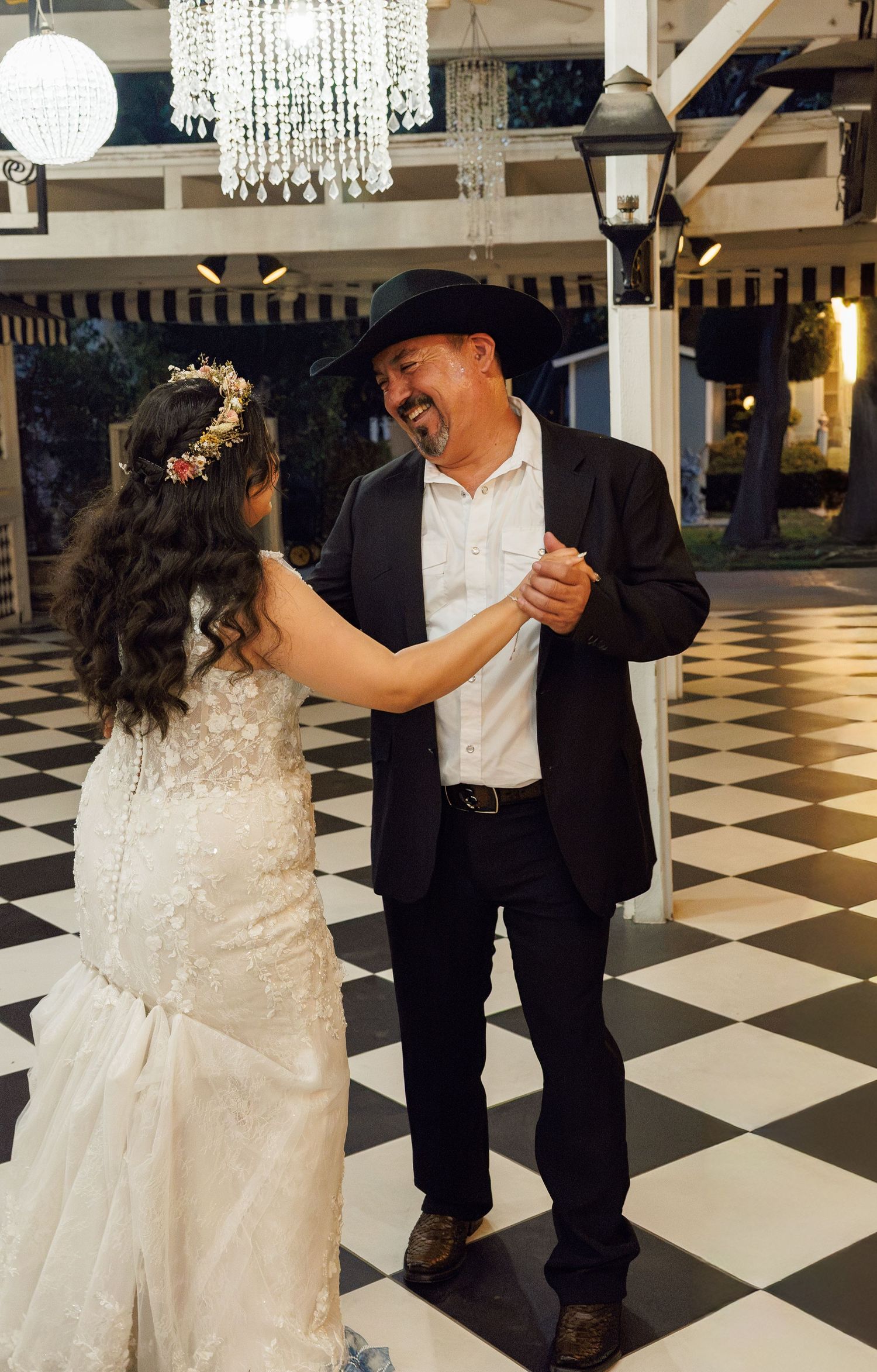 Father and daughter share a joyful dance on checkered floor at wedding reception.