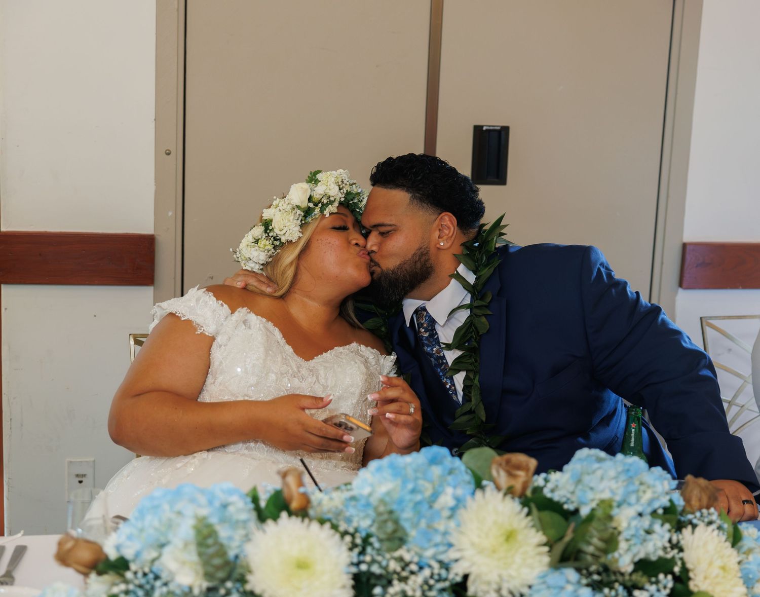 Bride and groom kissing at wedding reception table decorated with blue and white hydrangeas.