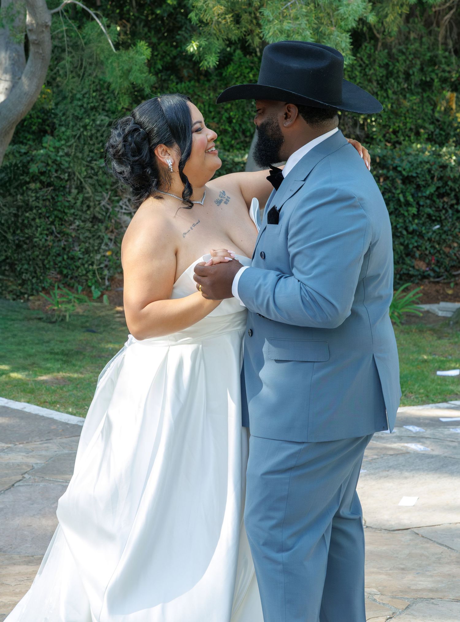 Bride and groom share first dance outdoors, groom wearing black cowboy hat and blue suit.