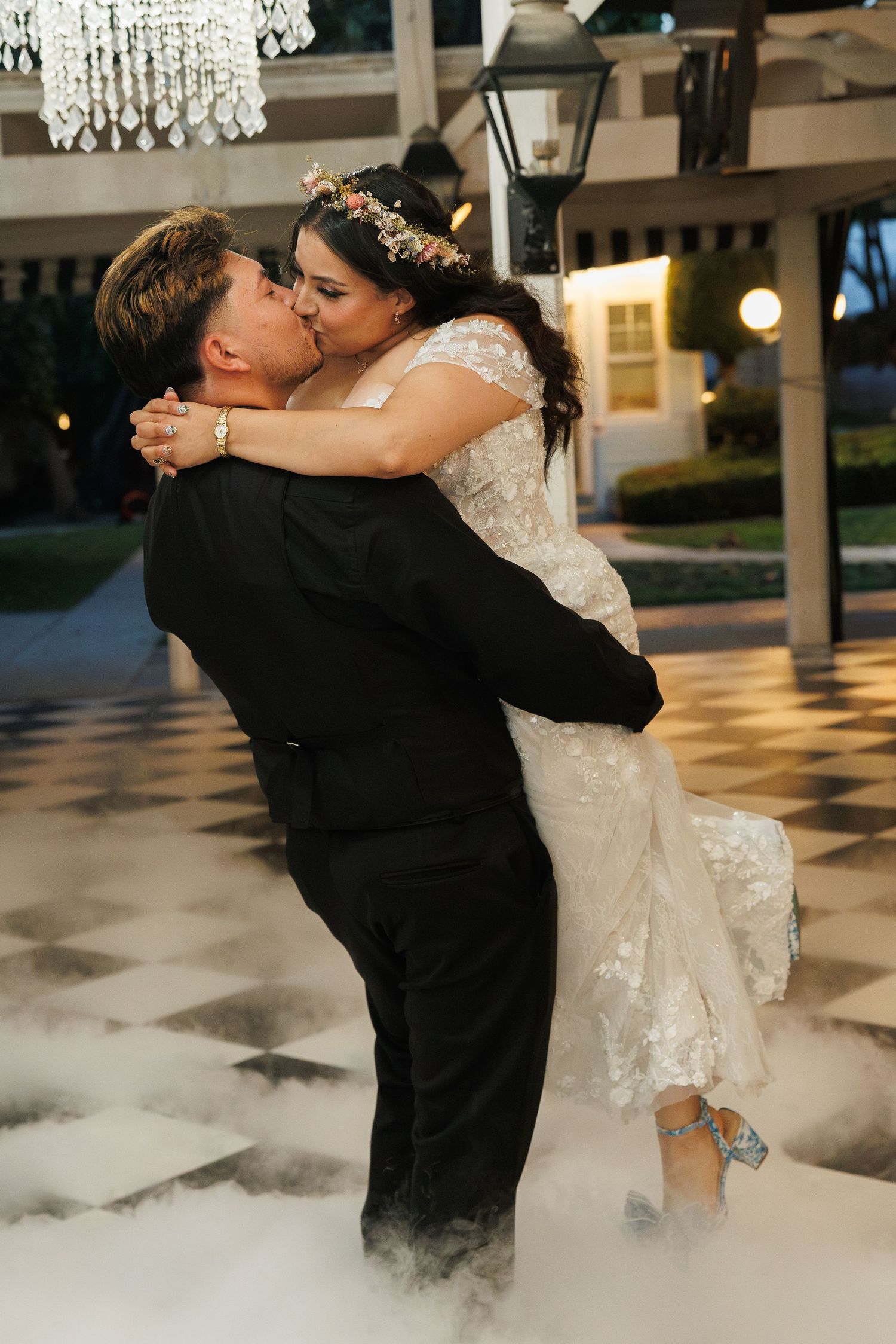Groom lifts bride for a kiss on a foggy dance floor at their elegant evening wedding reception.