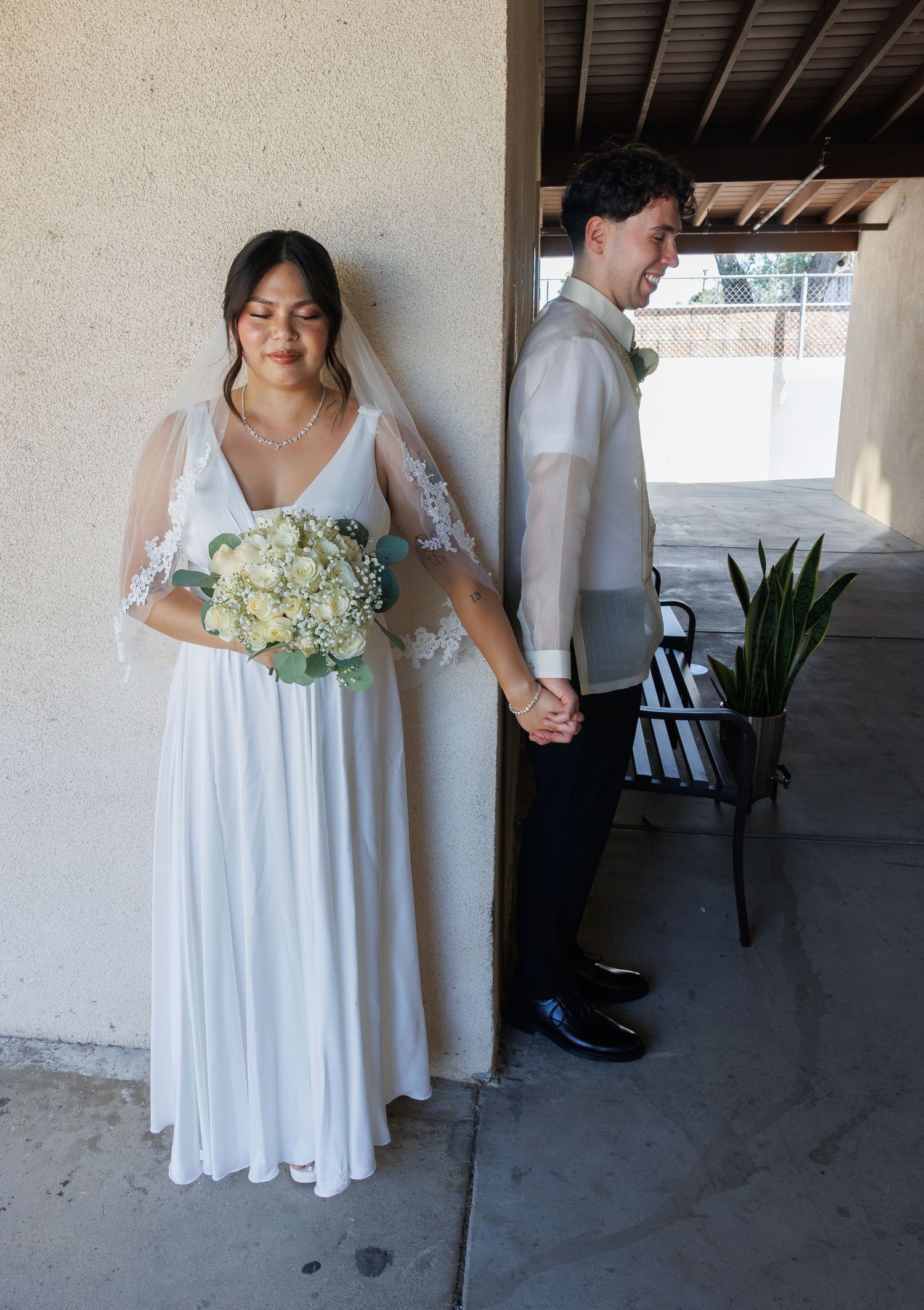 Bride in white gown holding bouquet stands with groom in barong tagalog, holding hands at their wedding ceremony.