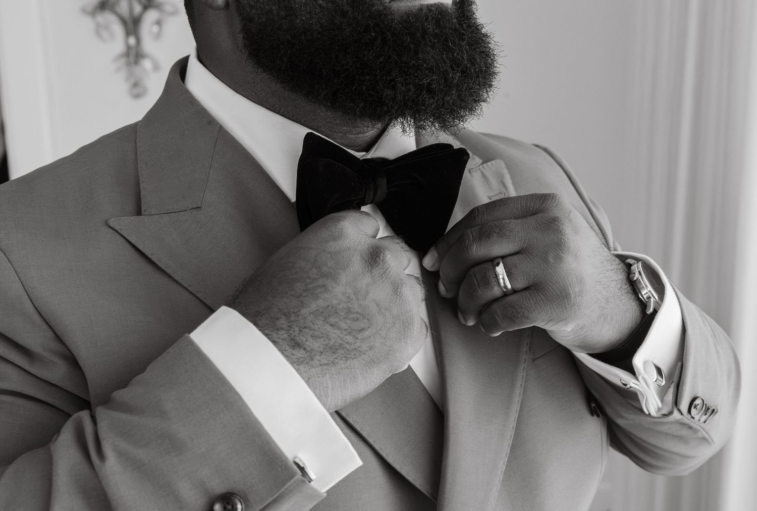 Close-up black and white photo of groom adjusting black bow tie with cufflinks visible.