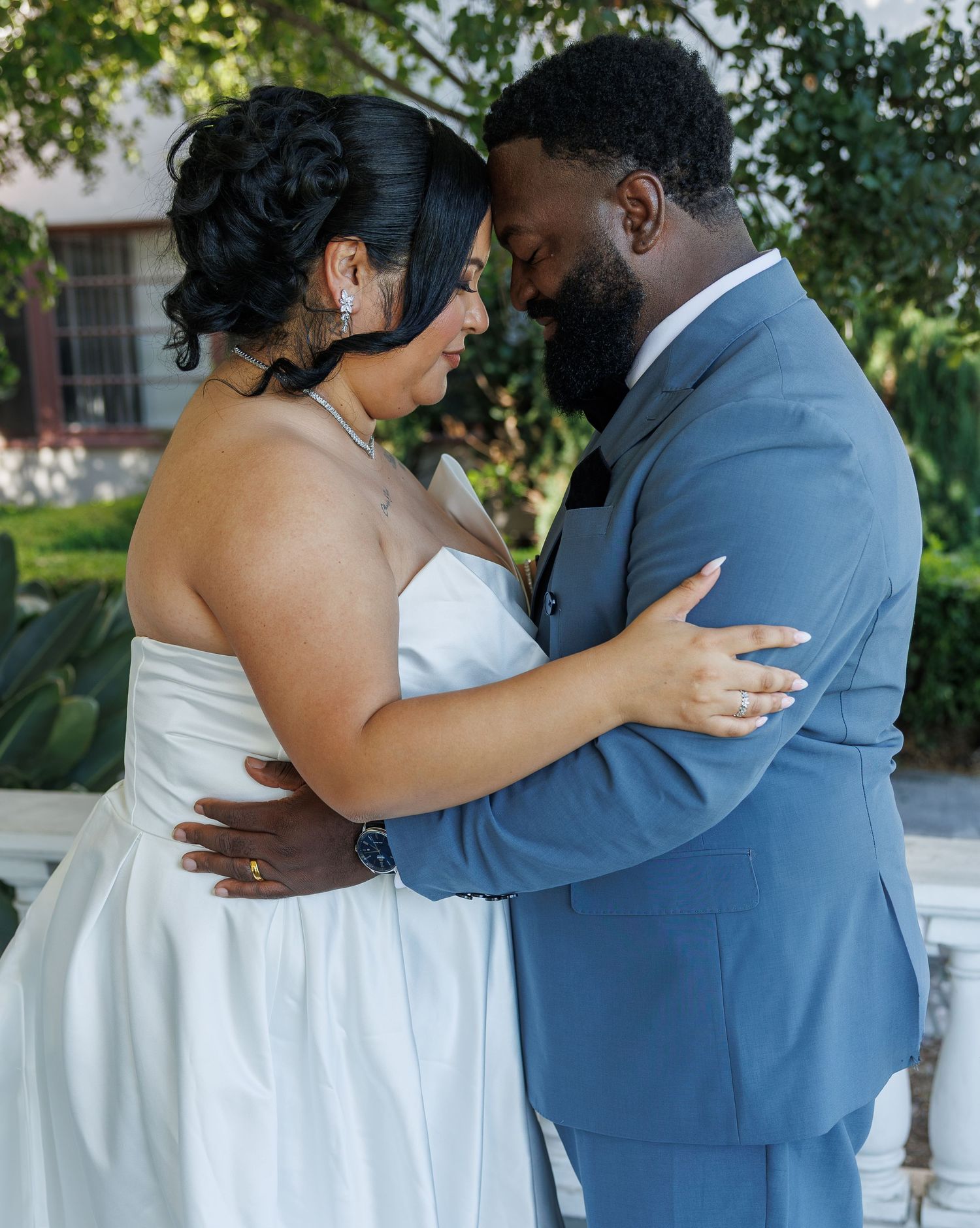 Bride and groom embracing forehead to forehead in tender moment at outdoor wedding.