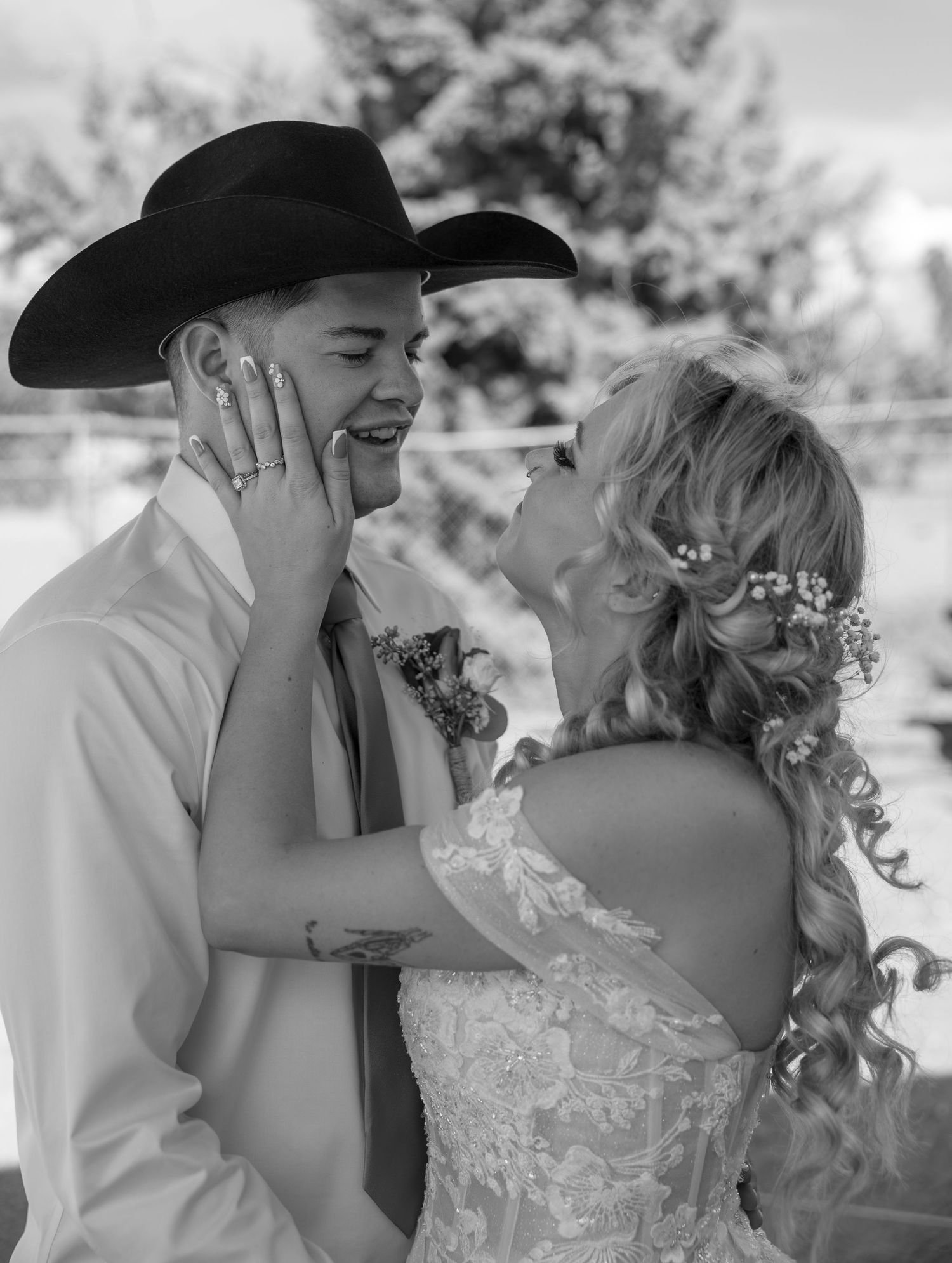 Black and white photo of smiling bride and groom in cowboy hat sharing tender moment at wedding.