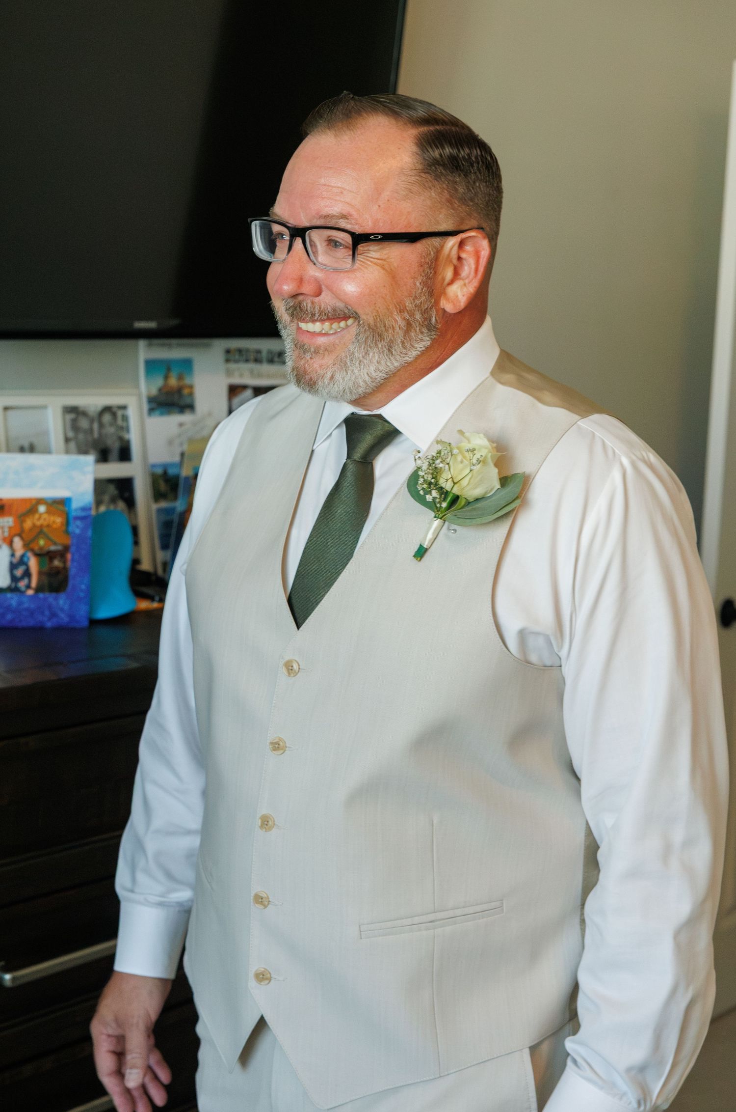 Smiling groom in white vest, green tie, and boutonniere, dressed for wedding day celebrations.