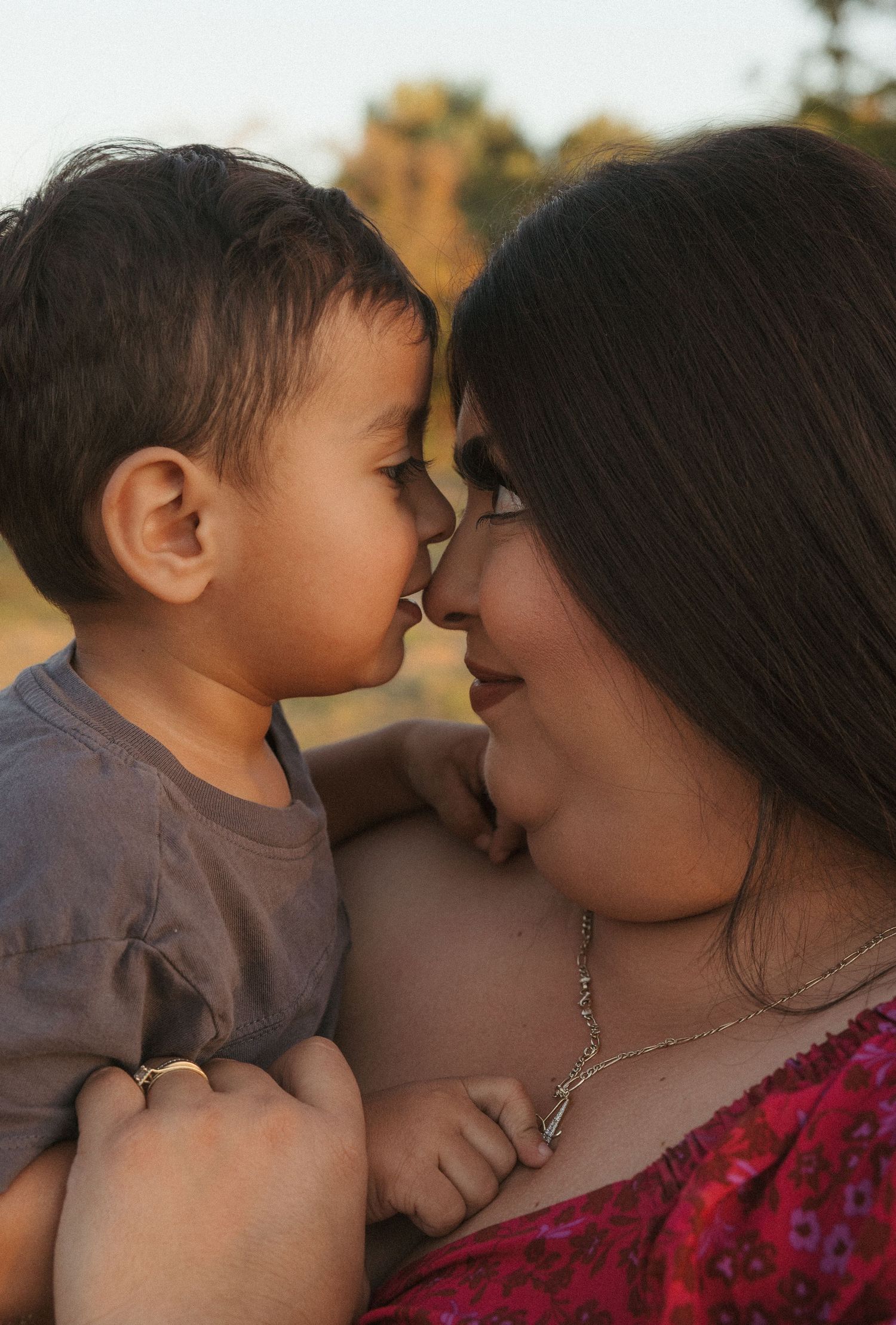 Mother and toddler touching noses affectionately outdoors in warm golden light.
