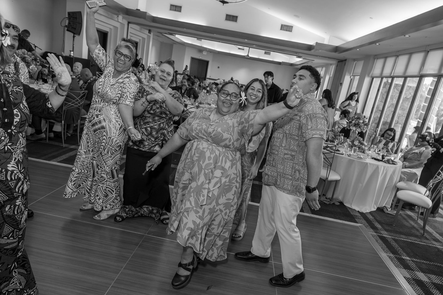 Guests dance joyfully at wedding reception in elegant venue, captured in black and white photography.