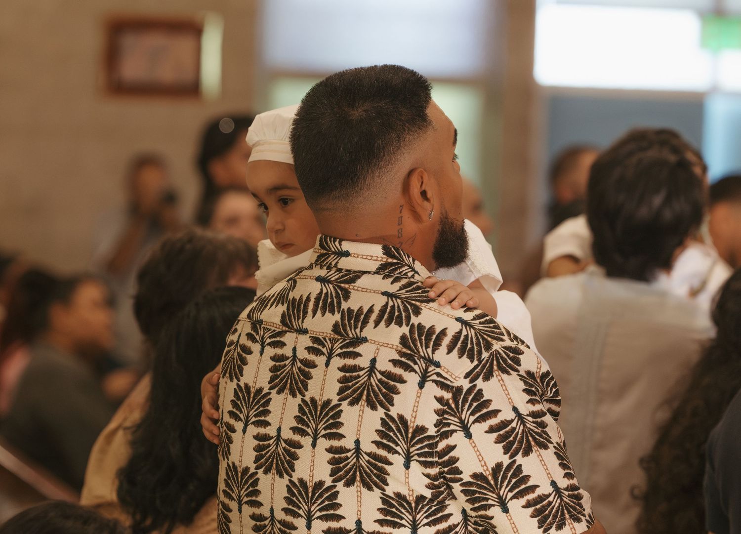 Two people embracing warmly in a crowded indoor gathering, one wearing a floral patterned shirt.