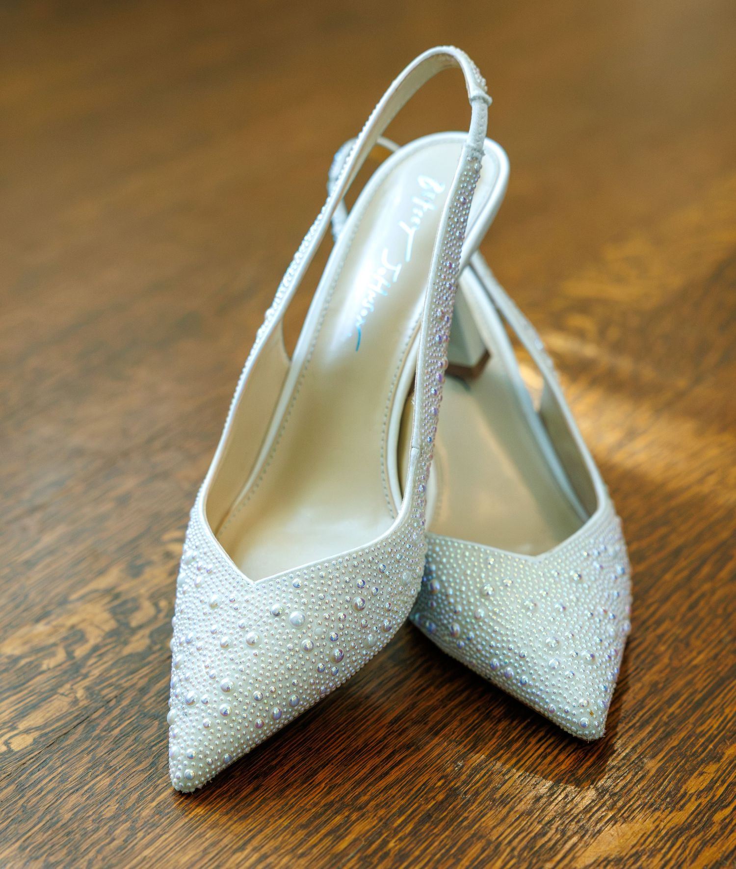 Elegant pearl-embellished white slingback bridal heels displayed on wooden floor.