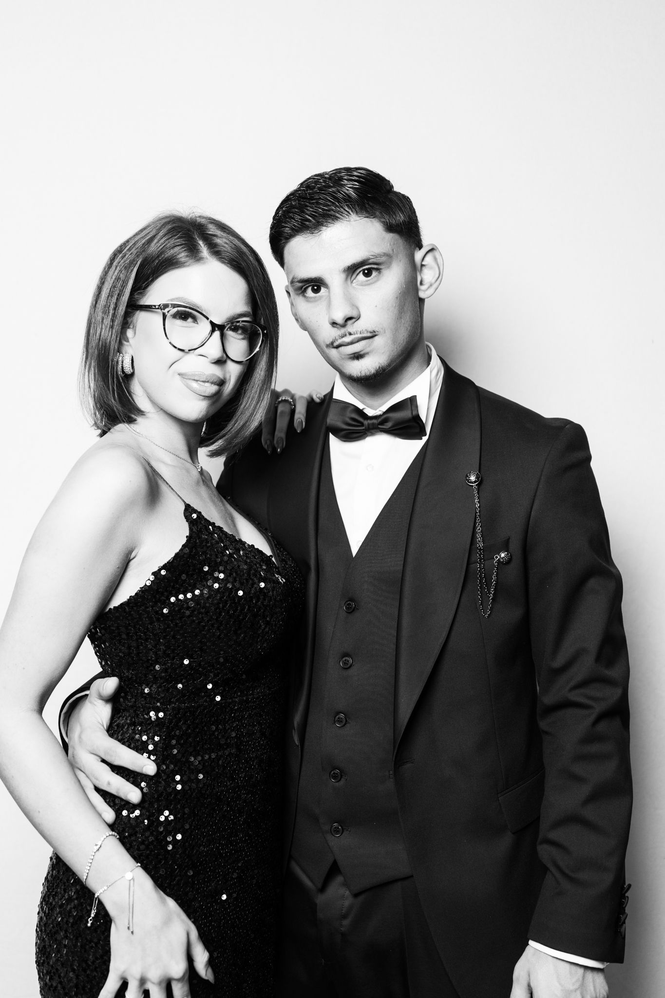 Elegant couple in black and white portrait, woman in sequin dress with glasses, man in tuxedo with bow tie.