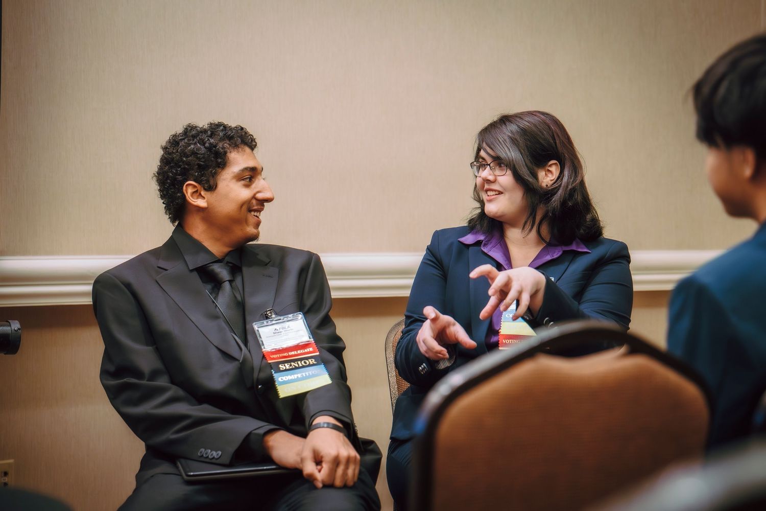 Two professionally dressed conference attendees wearing name badges engaged in conversation.