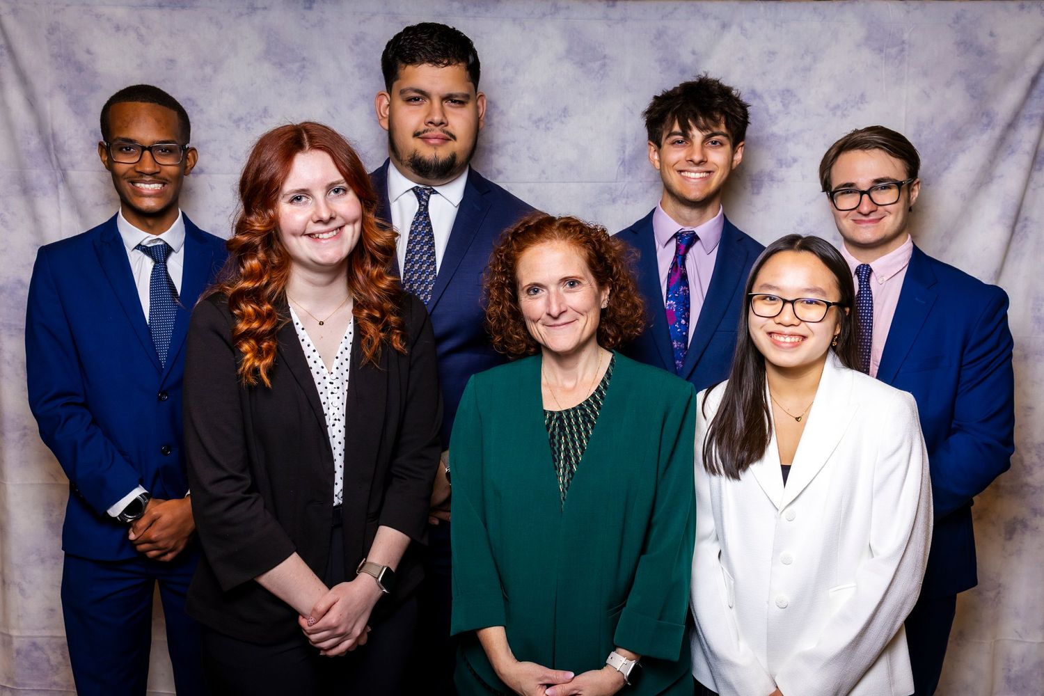 Group of seven diverse young professionals posing together at a formal business leadership event.