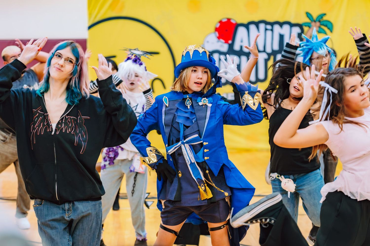 Cosplayers dancing on stage at an anime convention, featuring a blue pirate costume centerpiece.