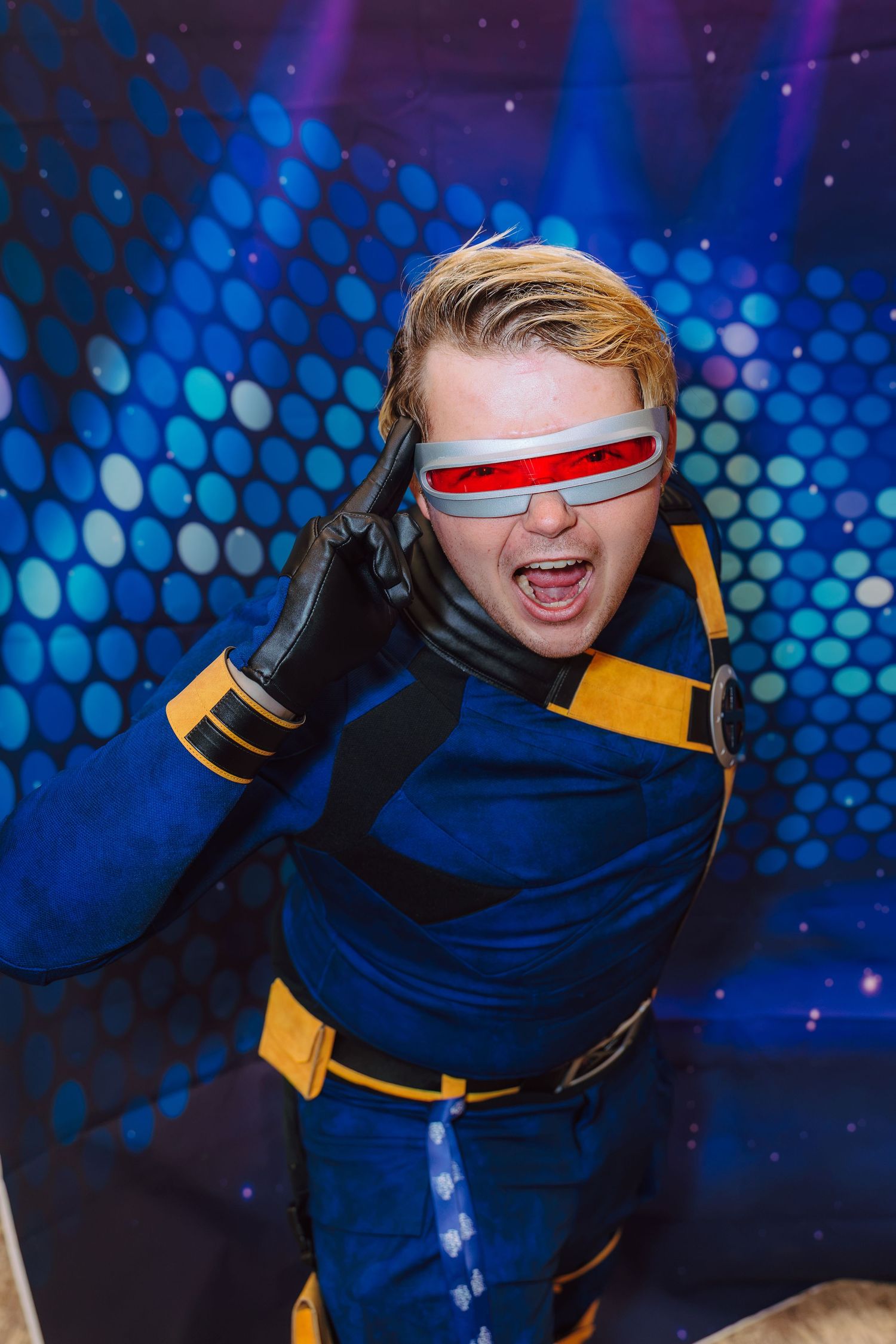 Person cosplaying as Cyclops from X-Men in blue and yellow suit with red visor, posing dramatically.