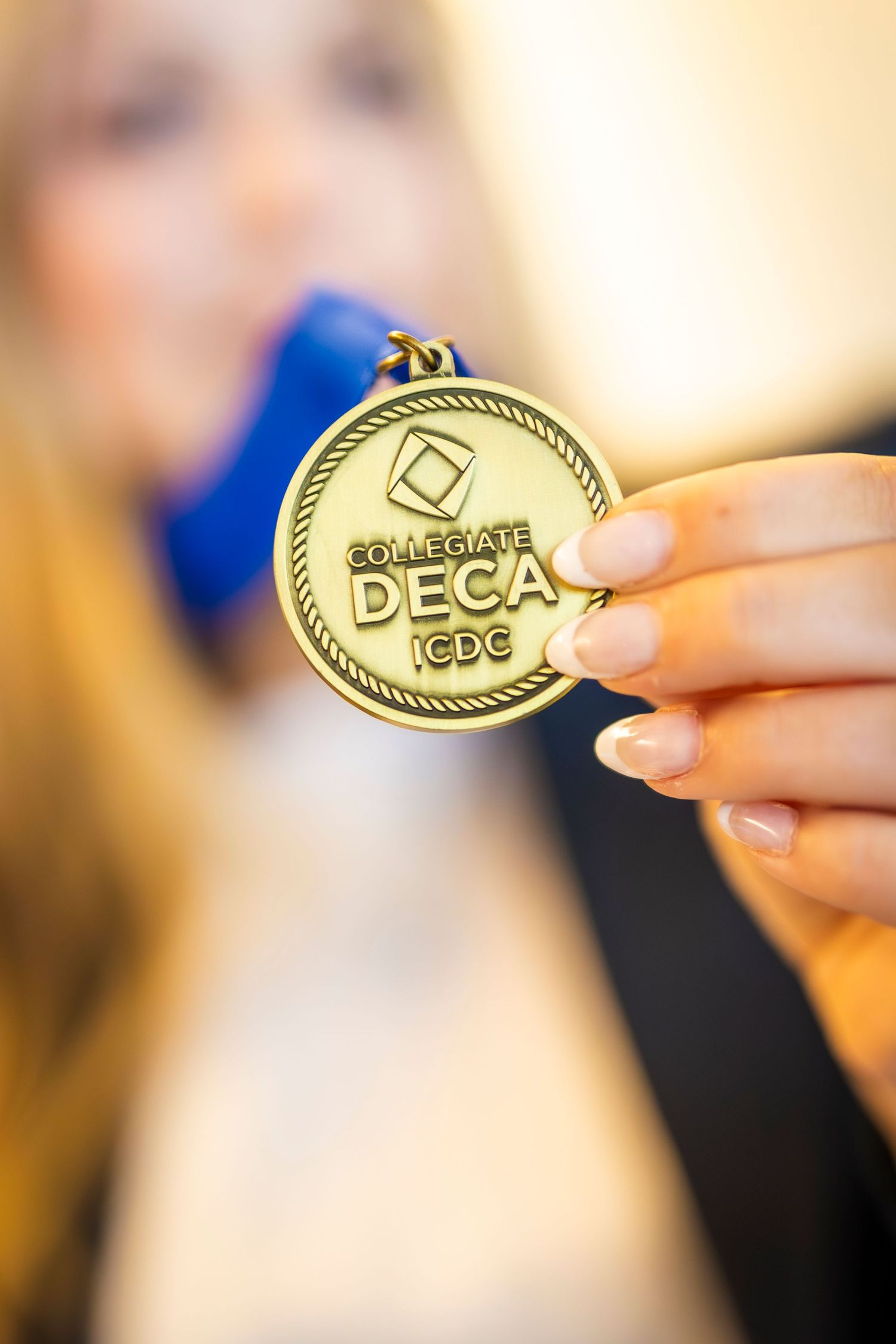 Hand holding a gold Collegiate DECA ICDC medal close to the camera.