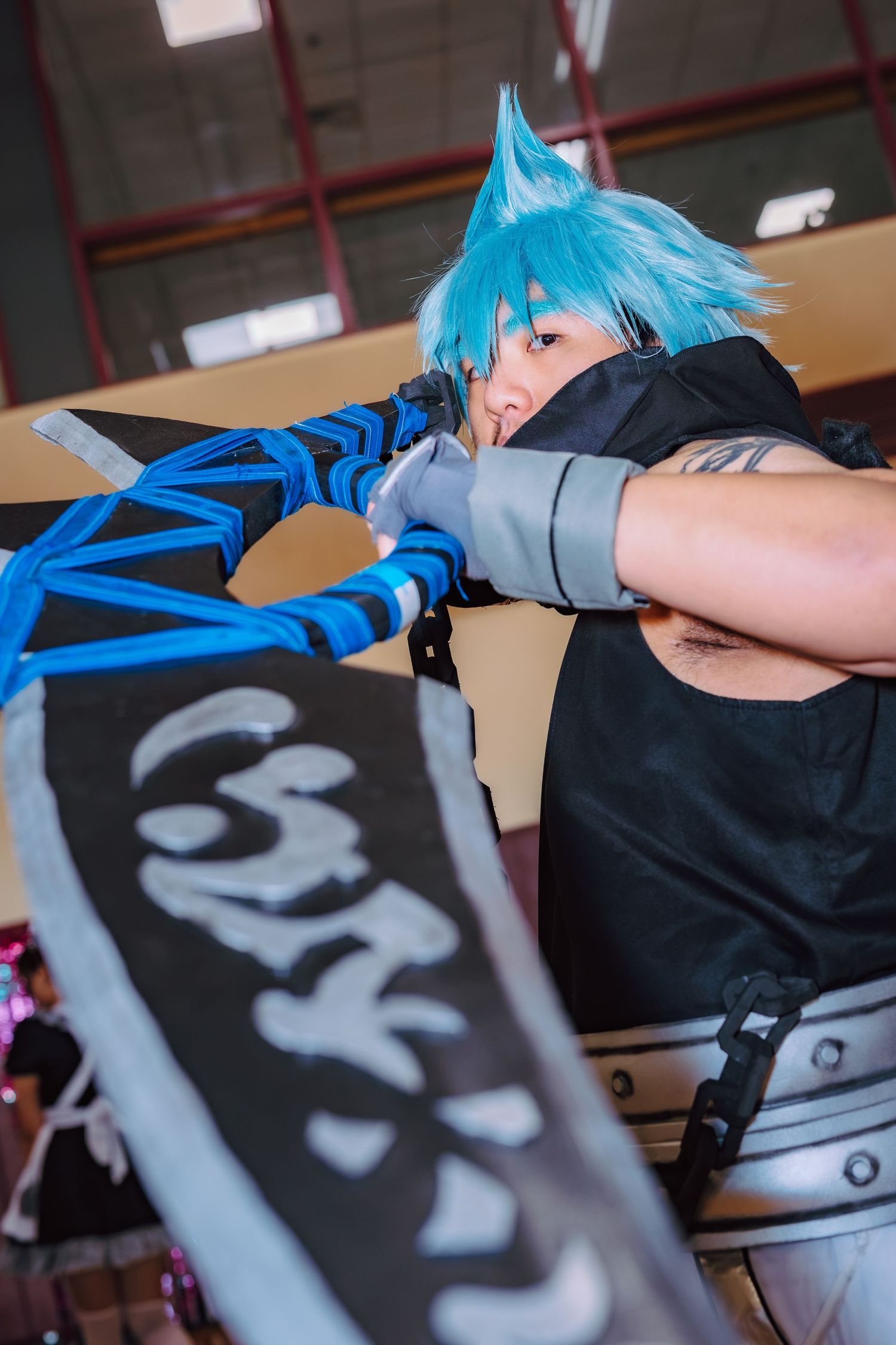Cosplayer with blue spiky hair wielding a large decorative sword in an action pose at a convention.