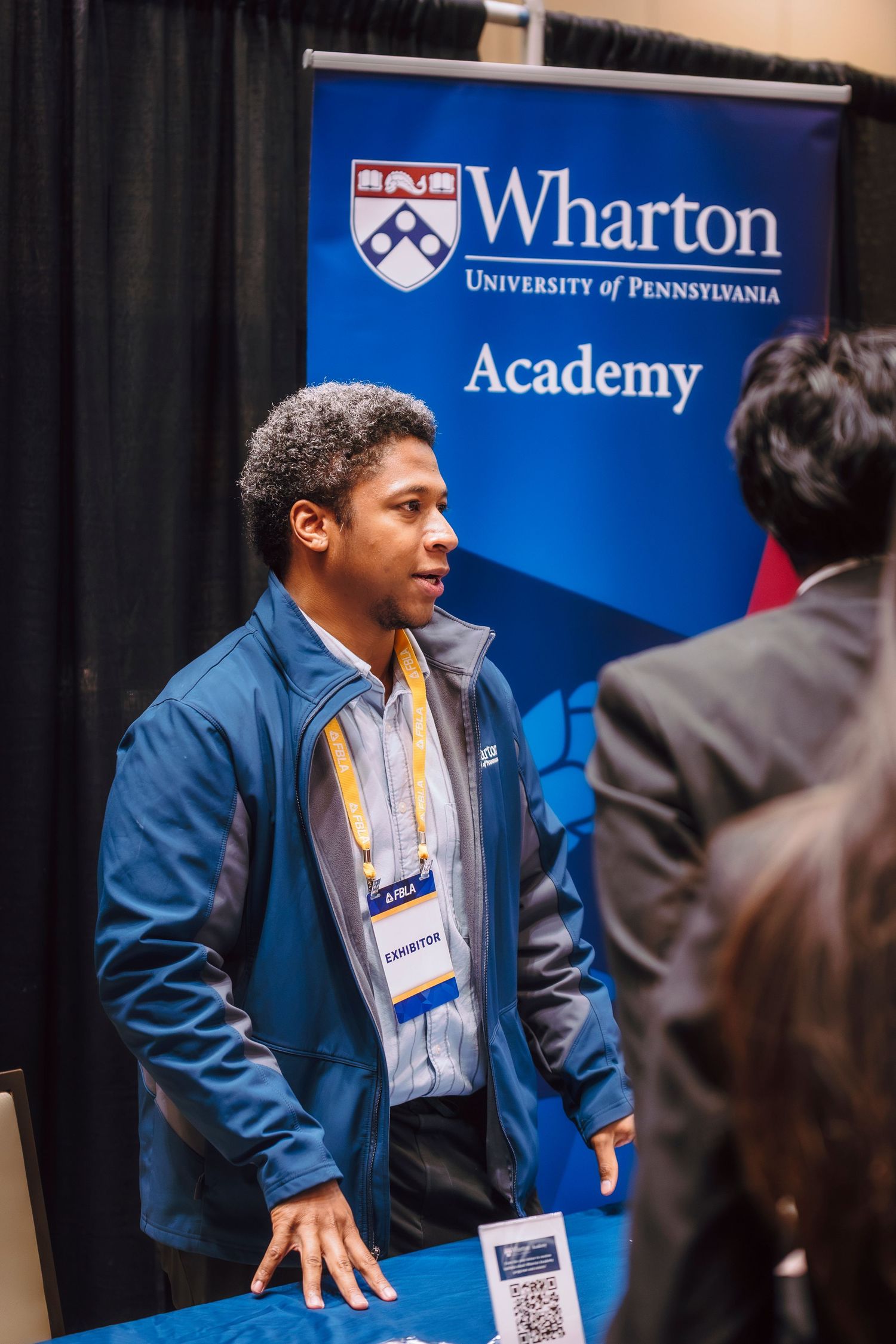 Young man in blue jacket representing Wharton Academy at a University of Pennsylvania conference booth.