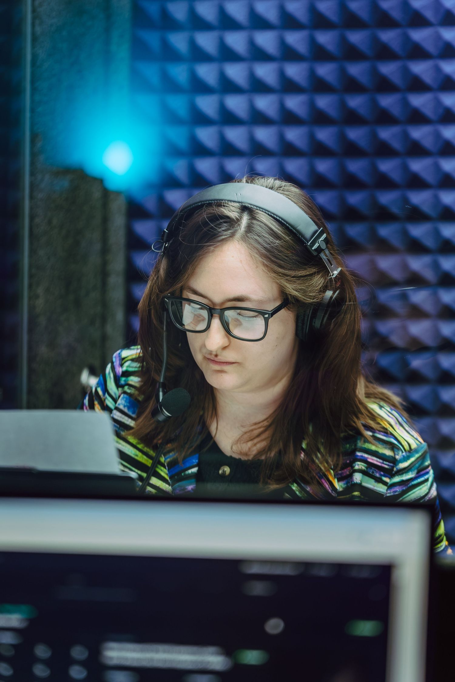 Young woman with glasses and headphones working at a computer in a professional recording studio.