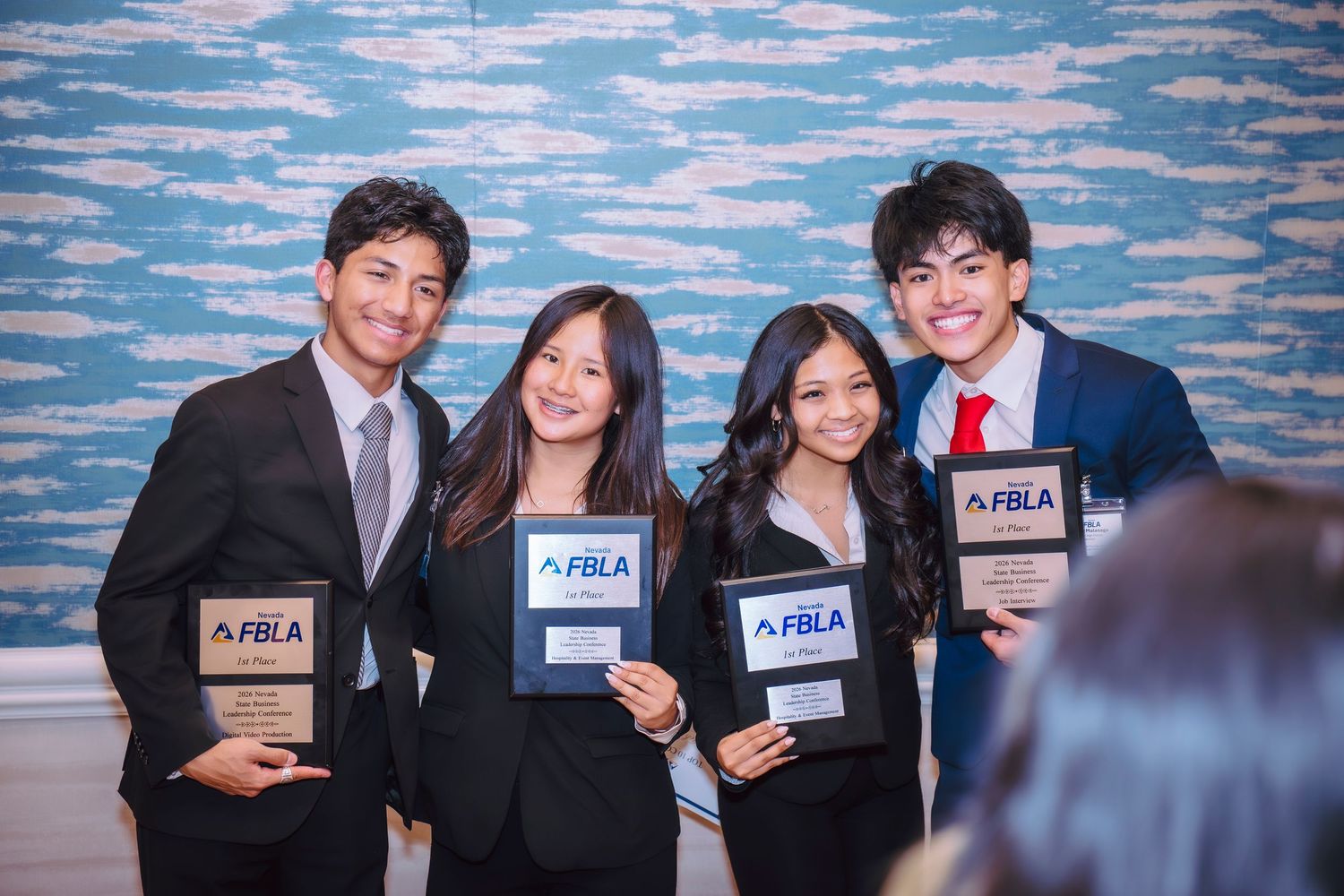 Four students in formal attire proudly hold FBLA awards at a business leadership competition event.