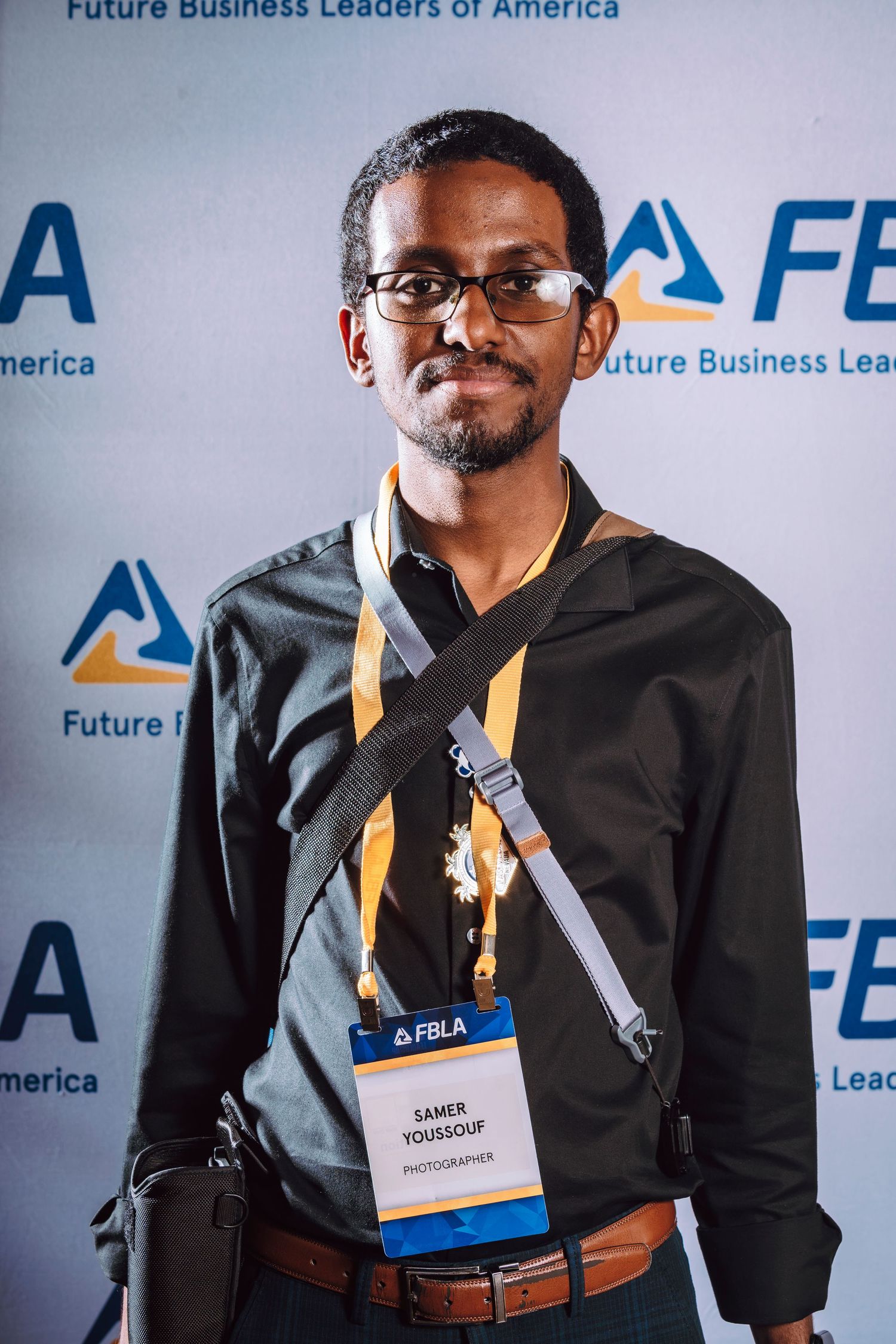 Young man in black shirt with FBLA photographer badge poses at Future Business Leaders of America event.