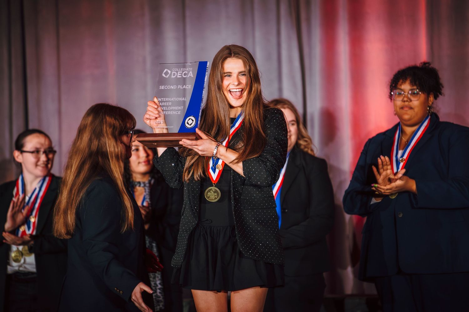 Student holding a DECA award trophy on stage with medal at a competition ceremony.