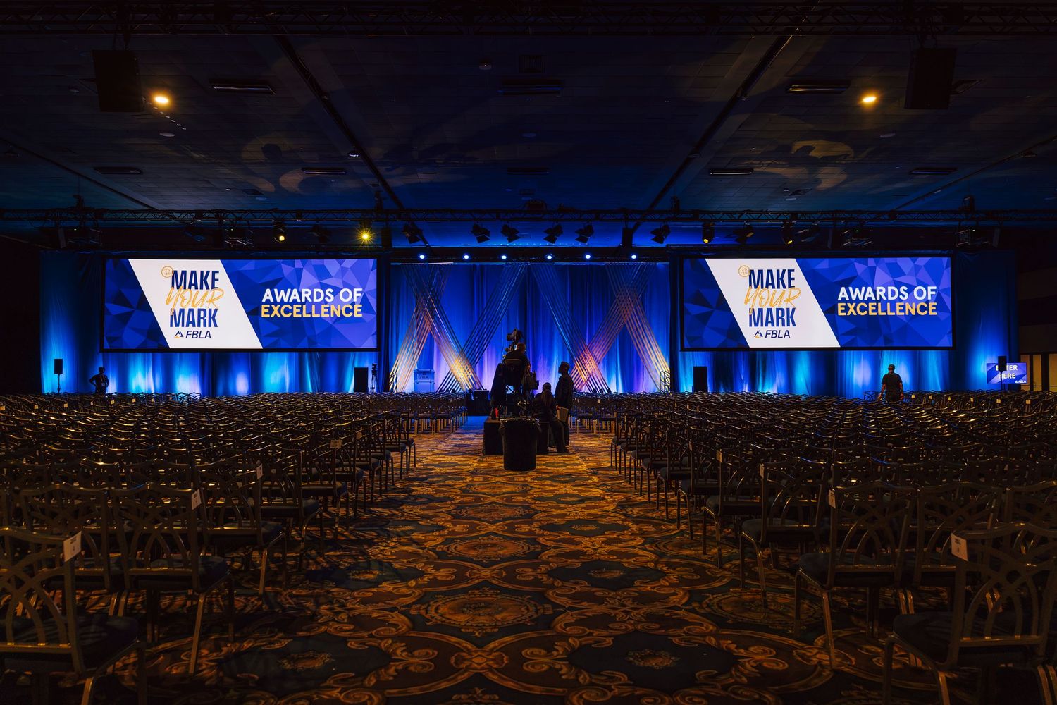 Large conference hall set up for DECA Awards of Excellence ceremony with blue stage lighting.