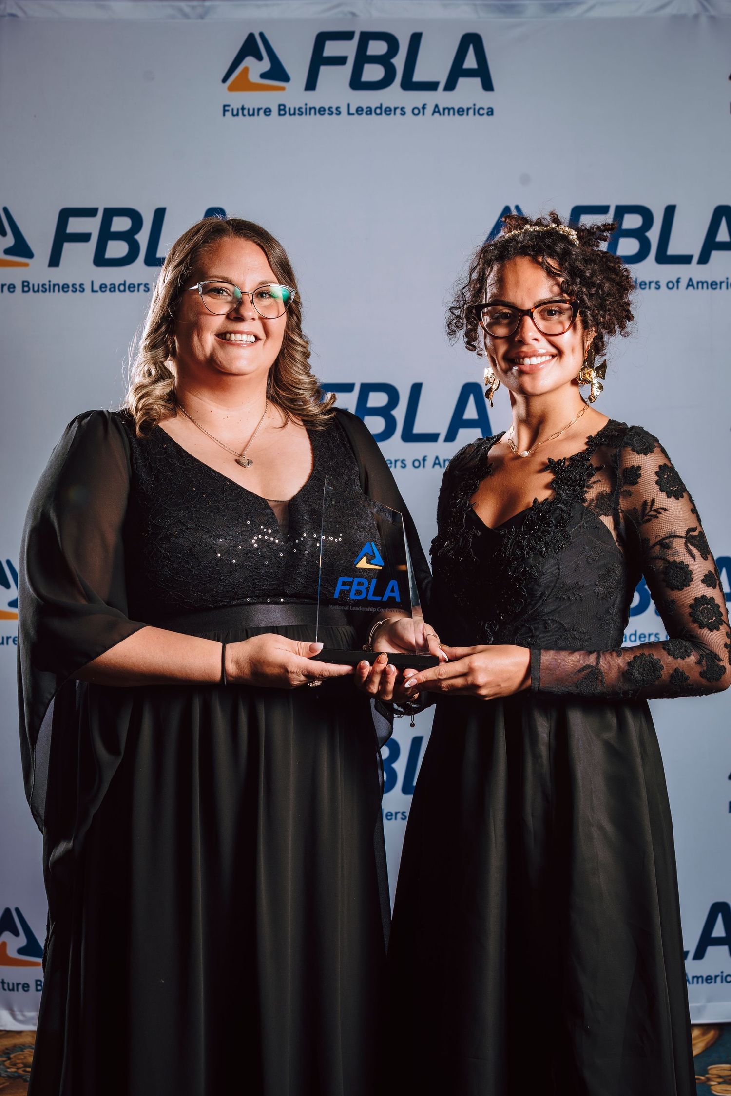 Two women in black dresses holding an FBLA award at a Future Business Leaders of America event.